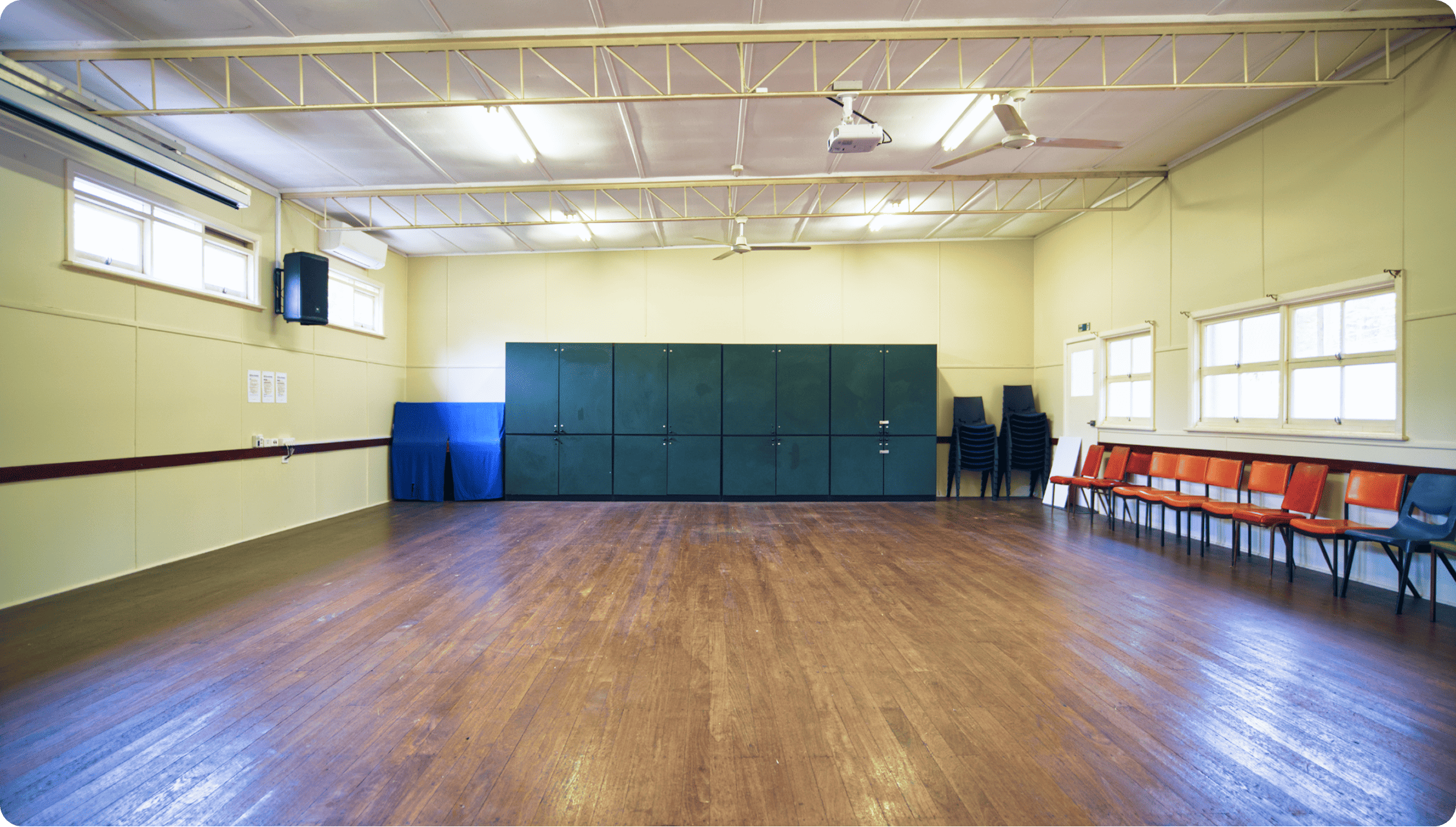 Bright hall with chairs stacked, a projector and cupboards