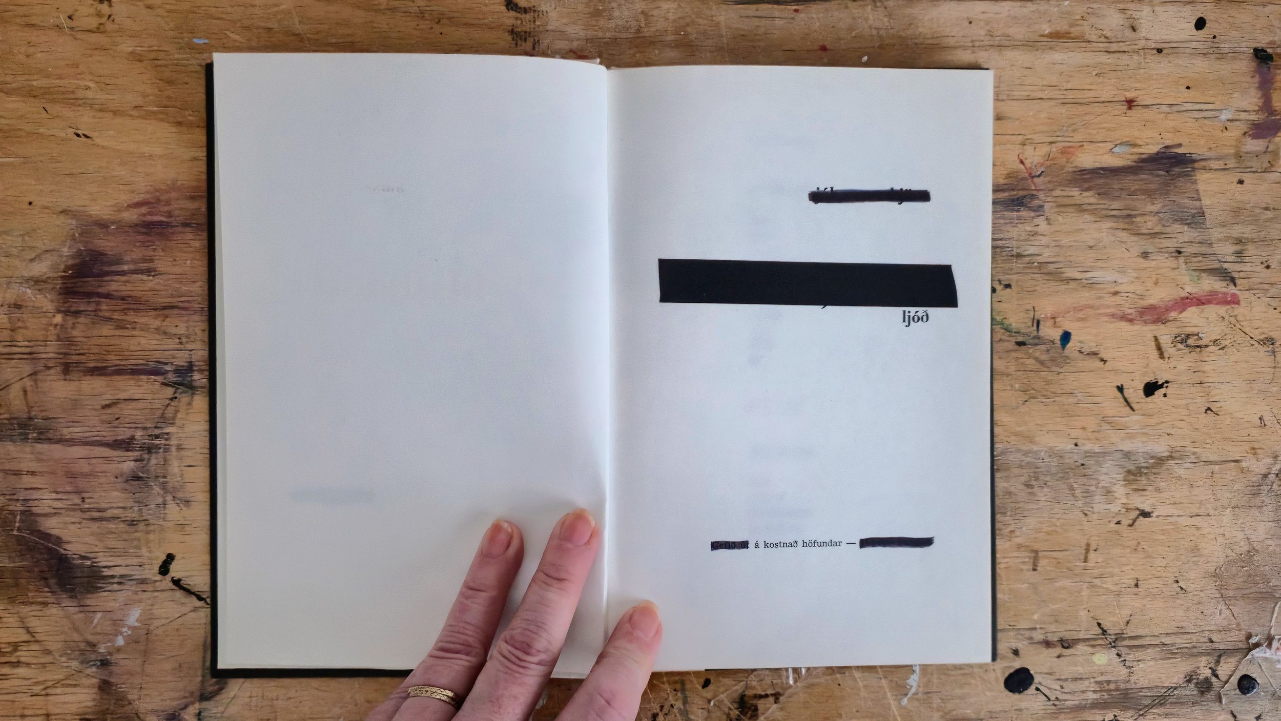 Open book on a wooden table, with a person's hand holding the bottom corner of the page.