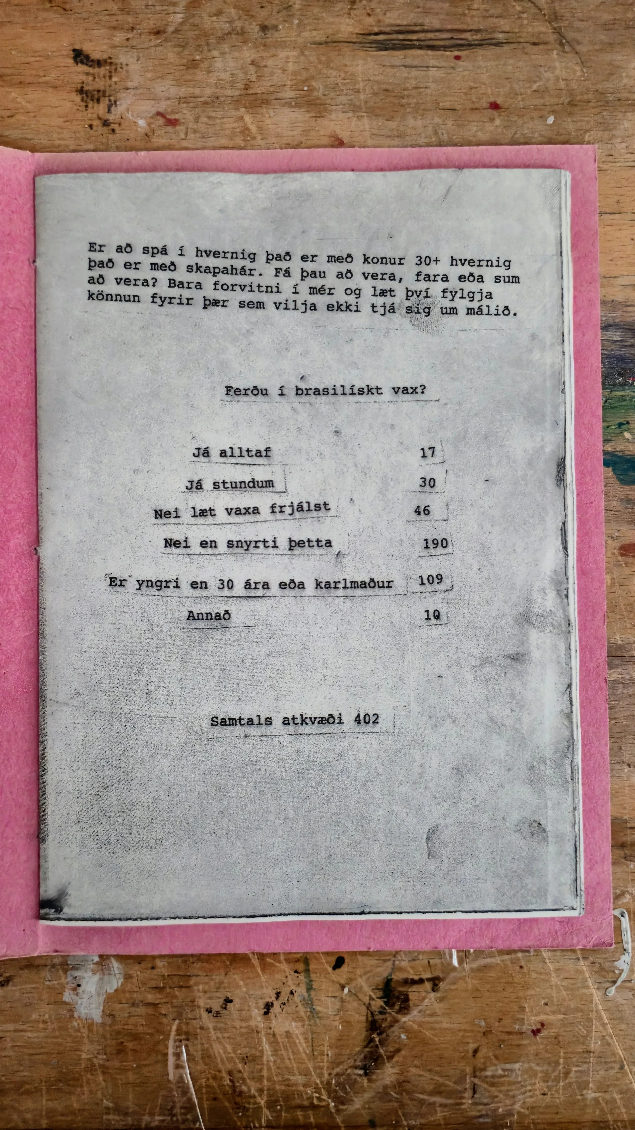 A printed note in Icelandic on a white paper sheet placed on a pink folder, lying on a wooden surface. The note discusses the stages of human development and contains a quiz with options and prices.