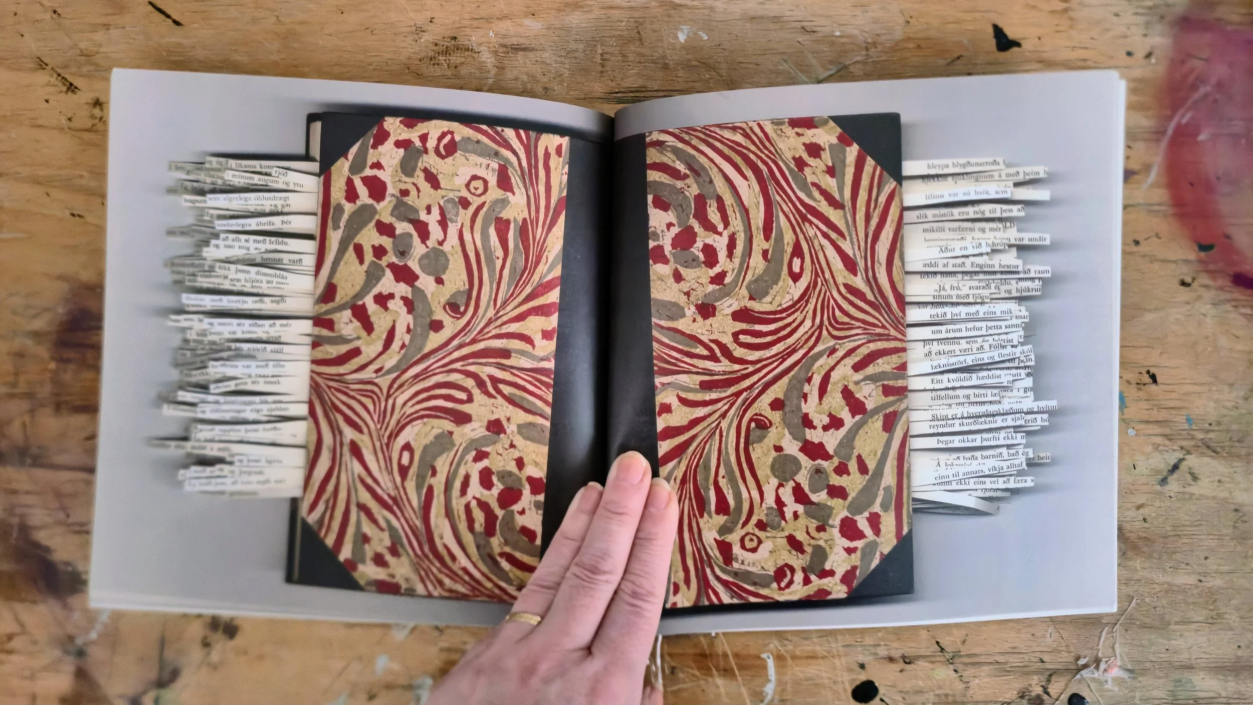 Open book with colorful abstract pattern on pages, held by hand, resting on a wooden surface.
