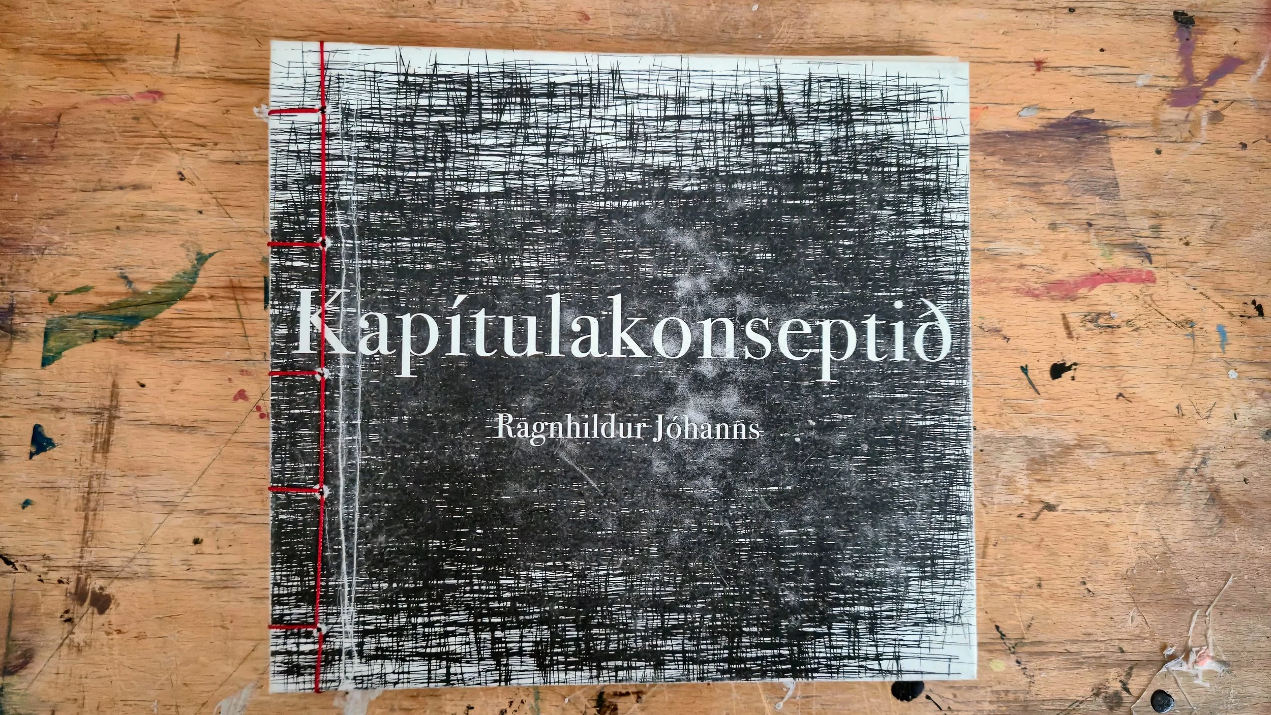 The cover of a book titled 'Kapitulakonsentio' by Ragnhildur Johanns, placed on a wooden surface with paint marks.
