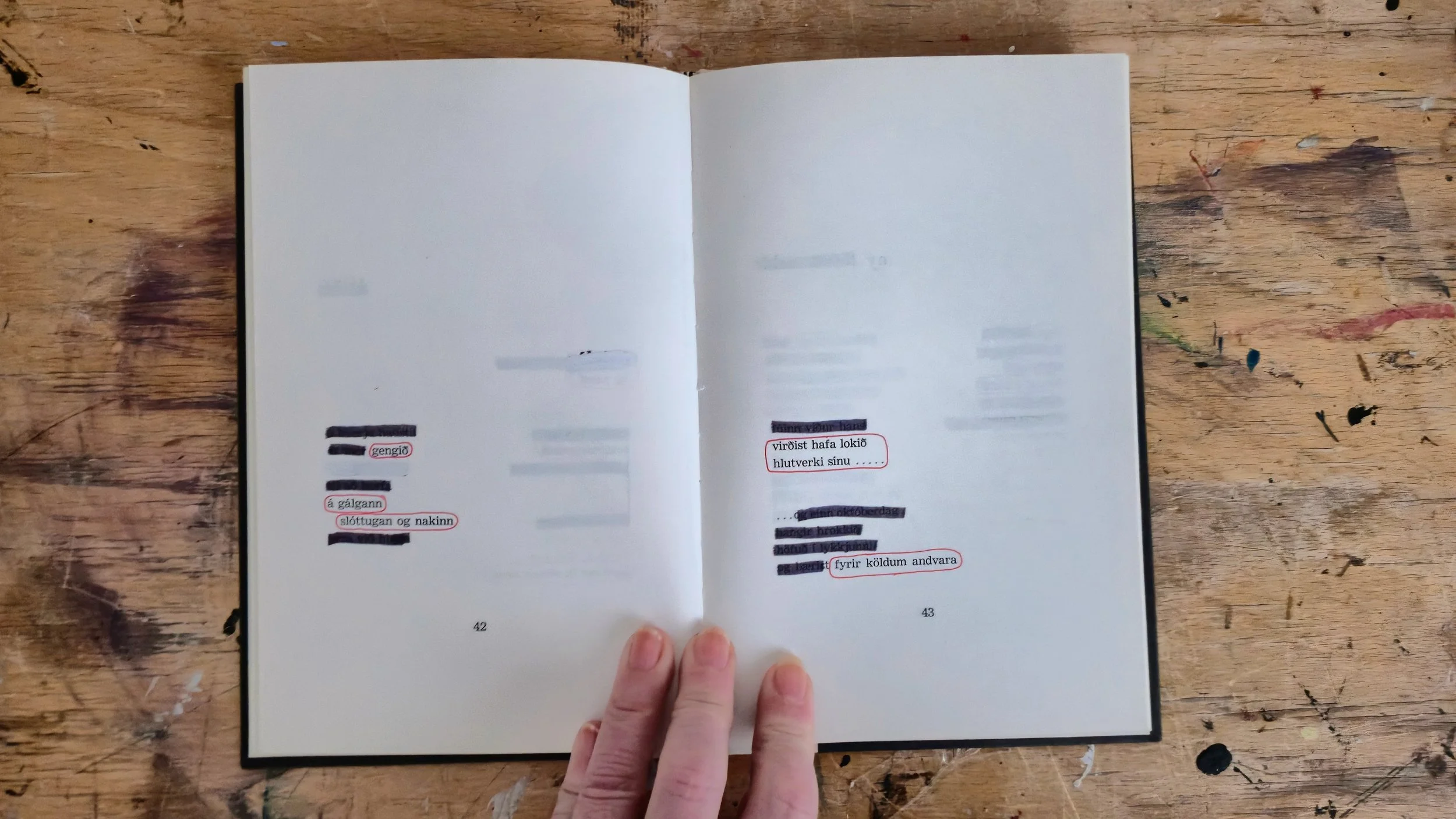 Open book on wooden surface, with handwritten or printed text highlighted in red, held by a person with visible fingers.