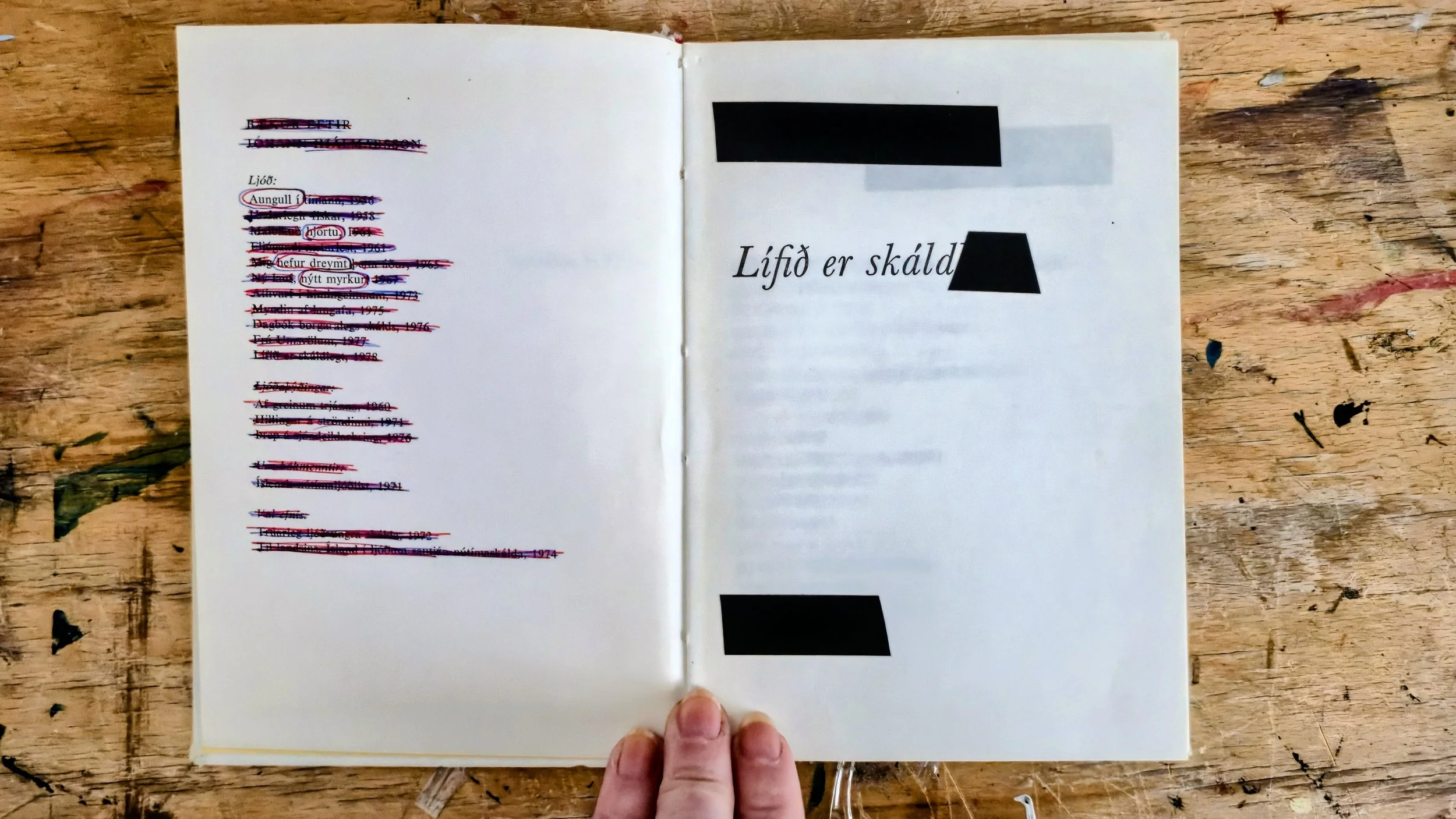 Open book on a wooden table with the Icelandic phrase "Lífið er skáldskapur" on the right page, and a list of items with names and dates crossed out on the left page.