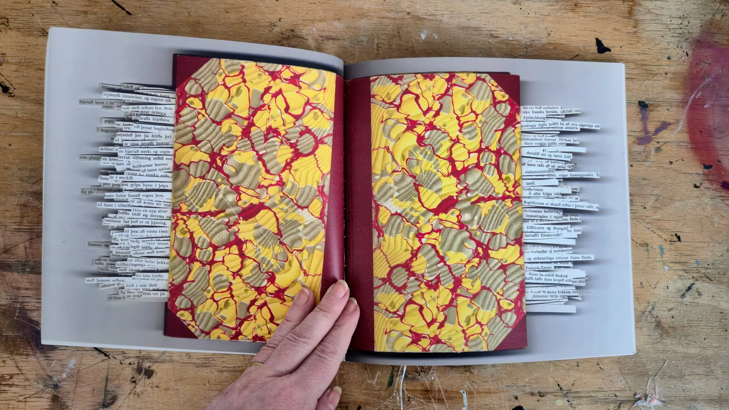 Open book on a wooden table with pages containing colorful abstract artwork and strips of text in a different language.