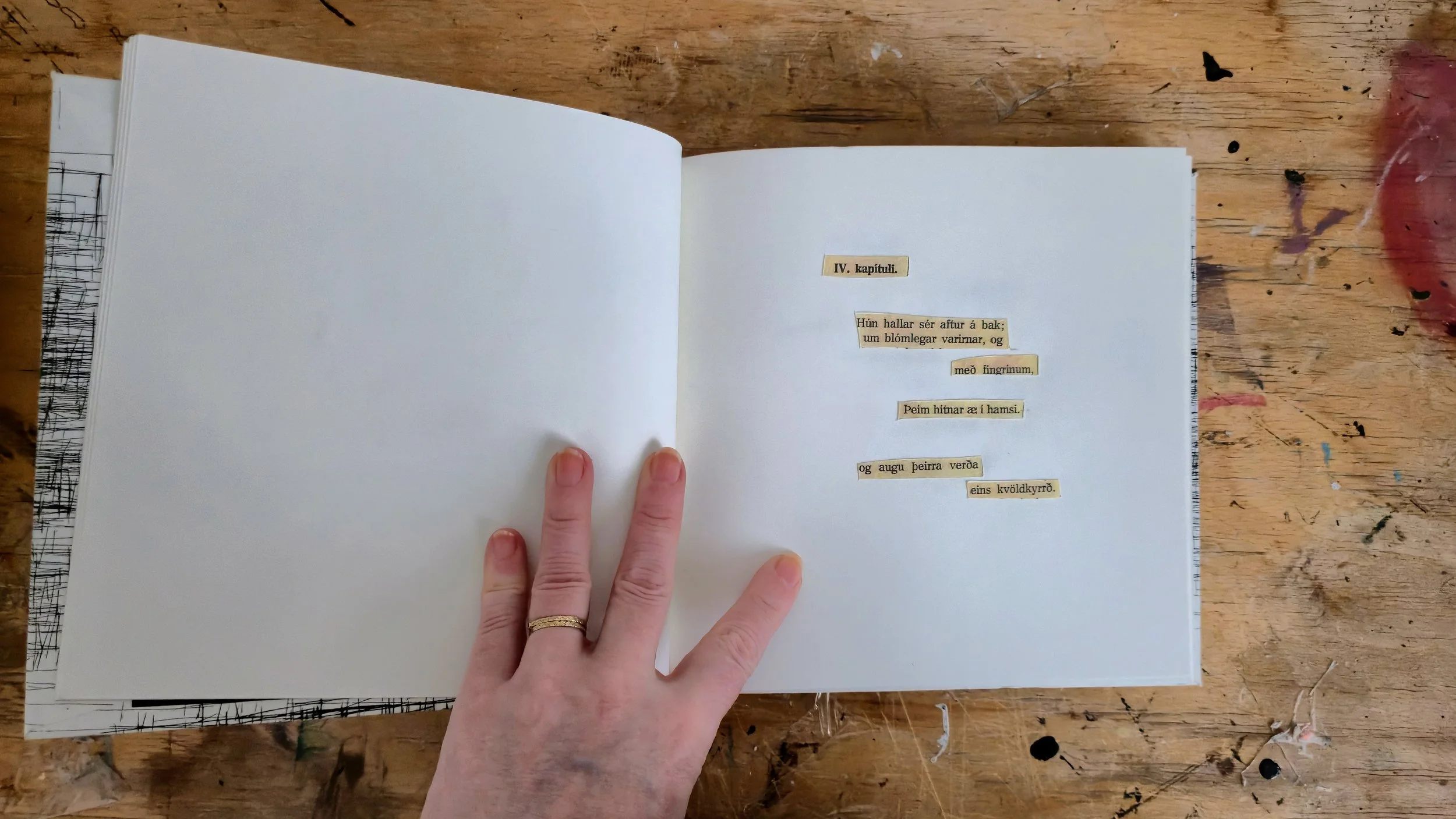 Open book on a wooden table with text in Icelandic, held by a person's hand.