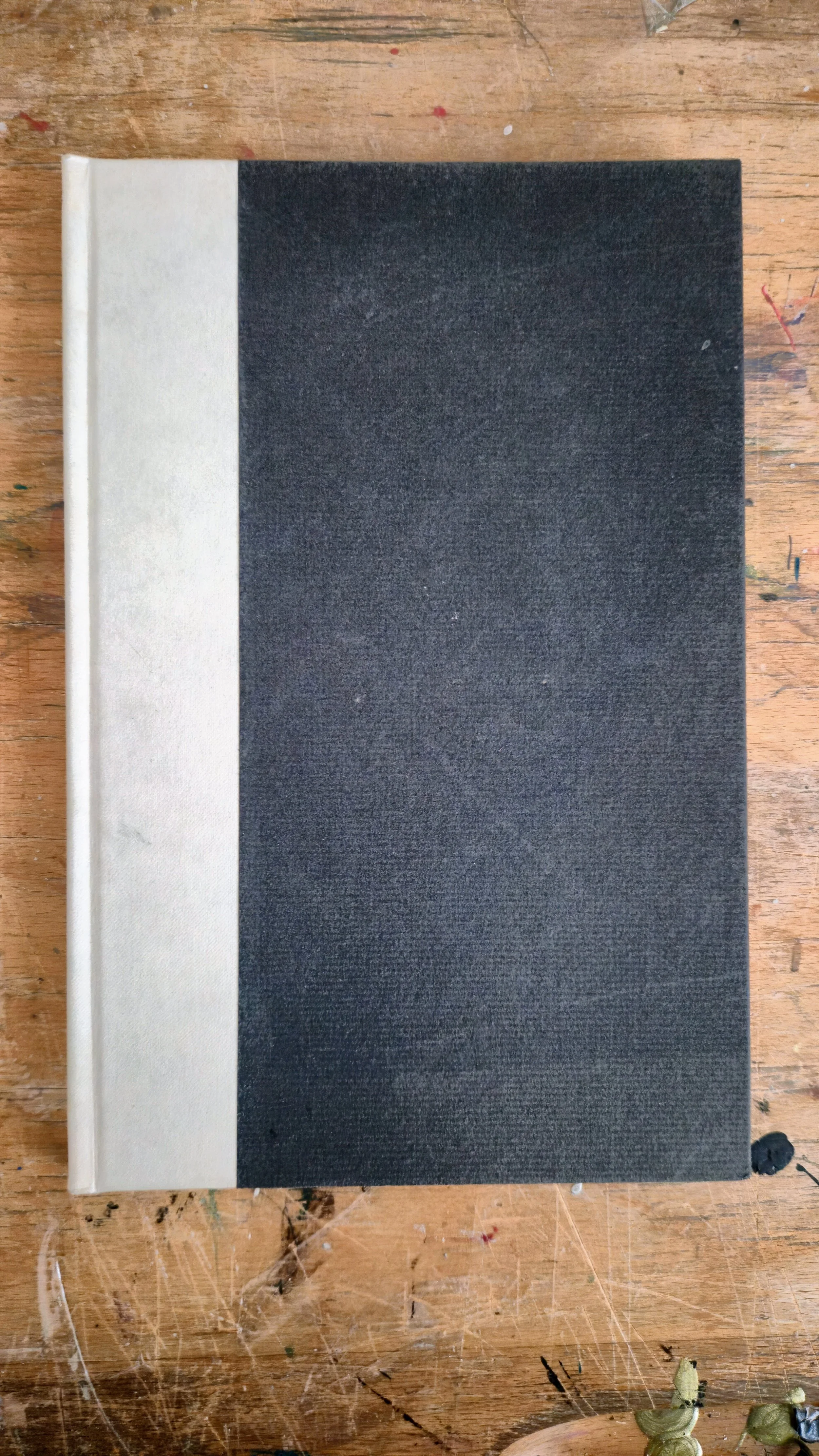 A closed hardcover book with a beige spine and a black cover, resting on a wooden surface.