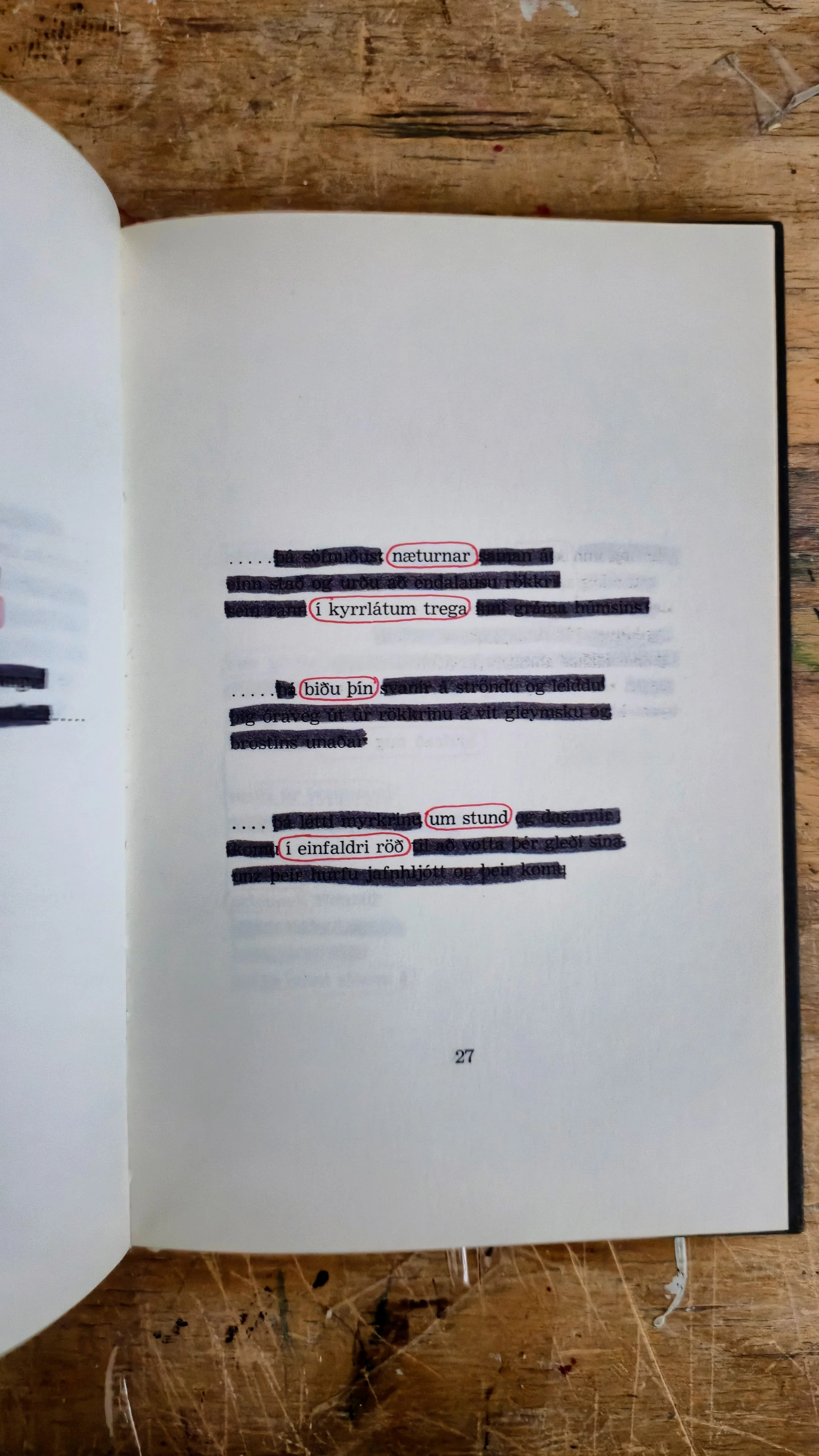 Open book on wooden table with highlighted and circled Icelandic words, page number 27.