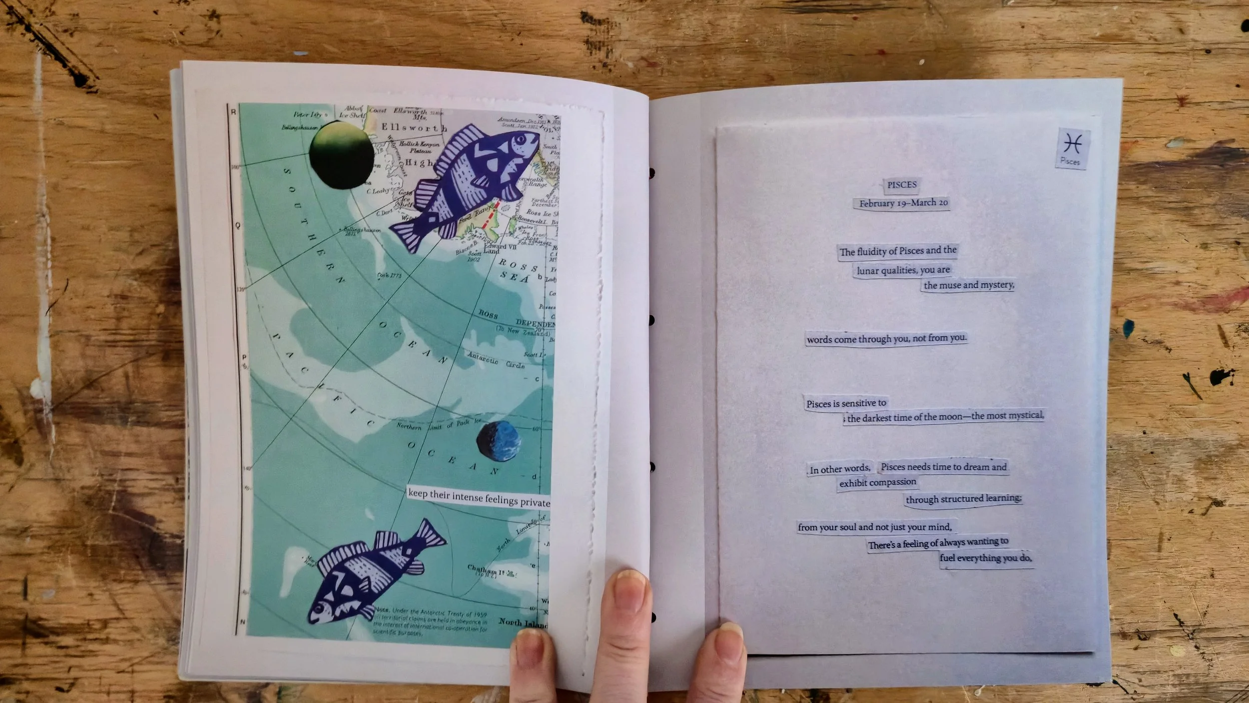 Open book on a wooden table showing a page with blue text about Pisces zodiac sign on the right and a map of the Ross Sea with illustrations of fish and the Earth on the left.