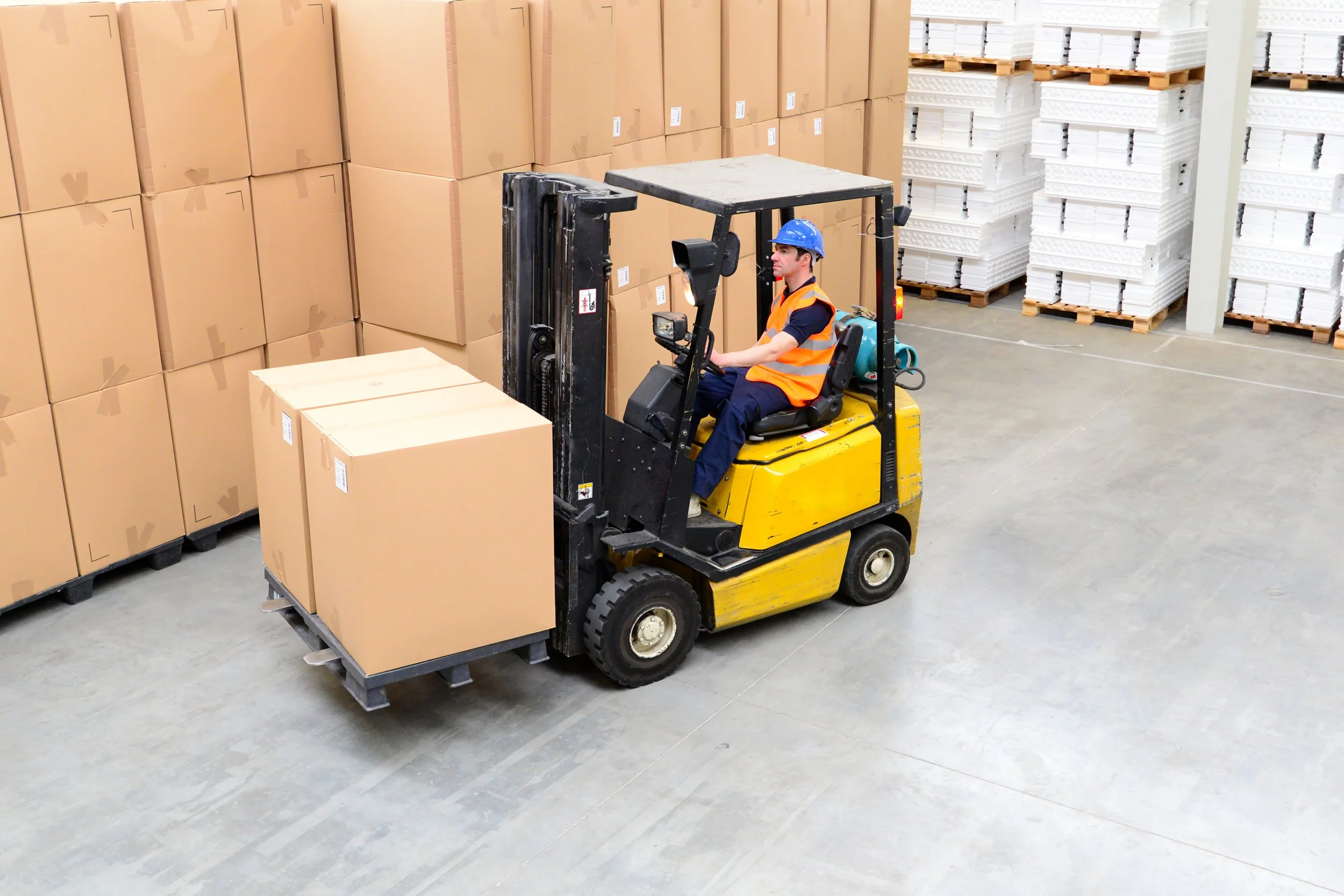 Warehouse forklift operator moving cardboard boxes.