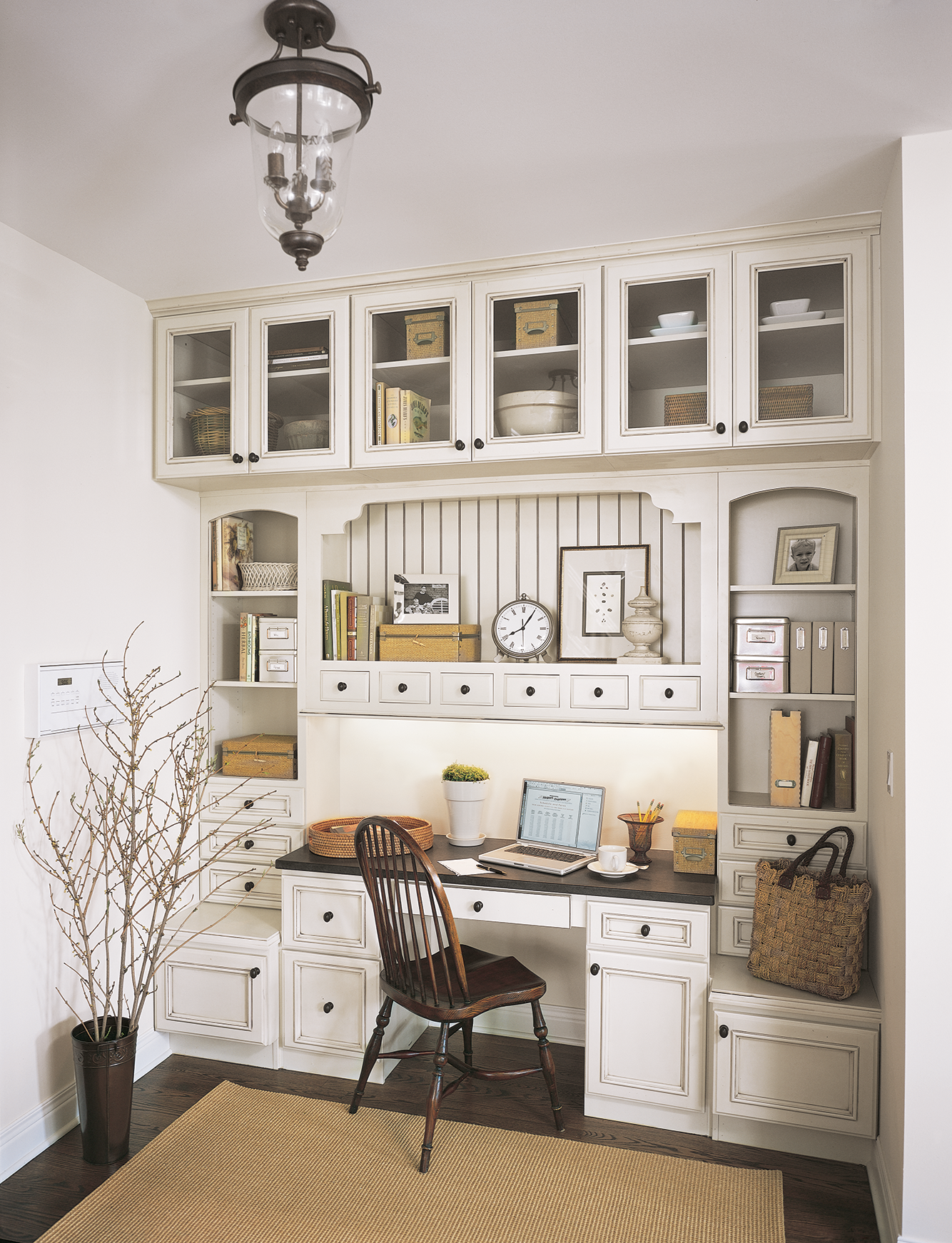 Home office with a wooden desk, white cabinets, laptop, books, and a decorative plant.