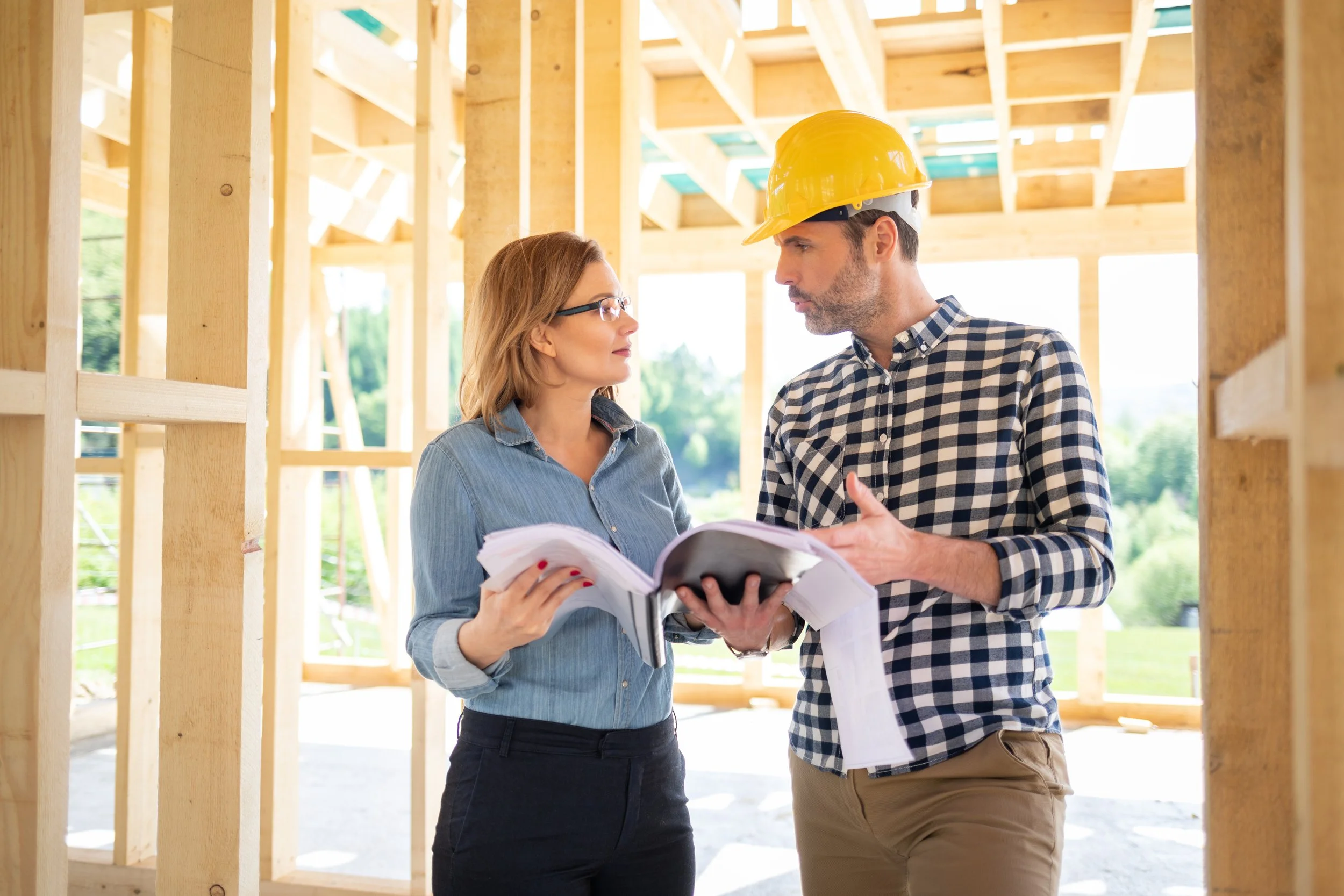 Two people discussing blueprints at a construction site with wooden framing.