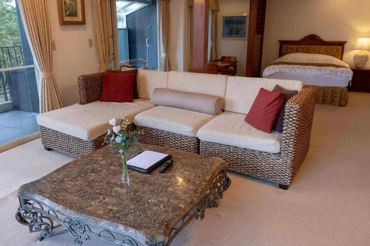 Elegantly decorated living room with wicker sofa, red cushions, marble coffee table, and a bed in the background.