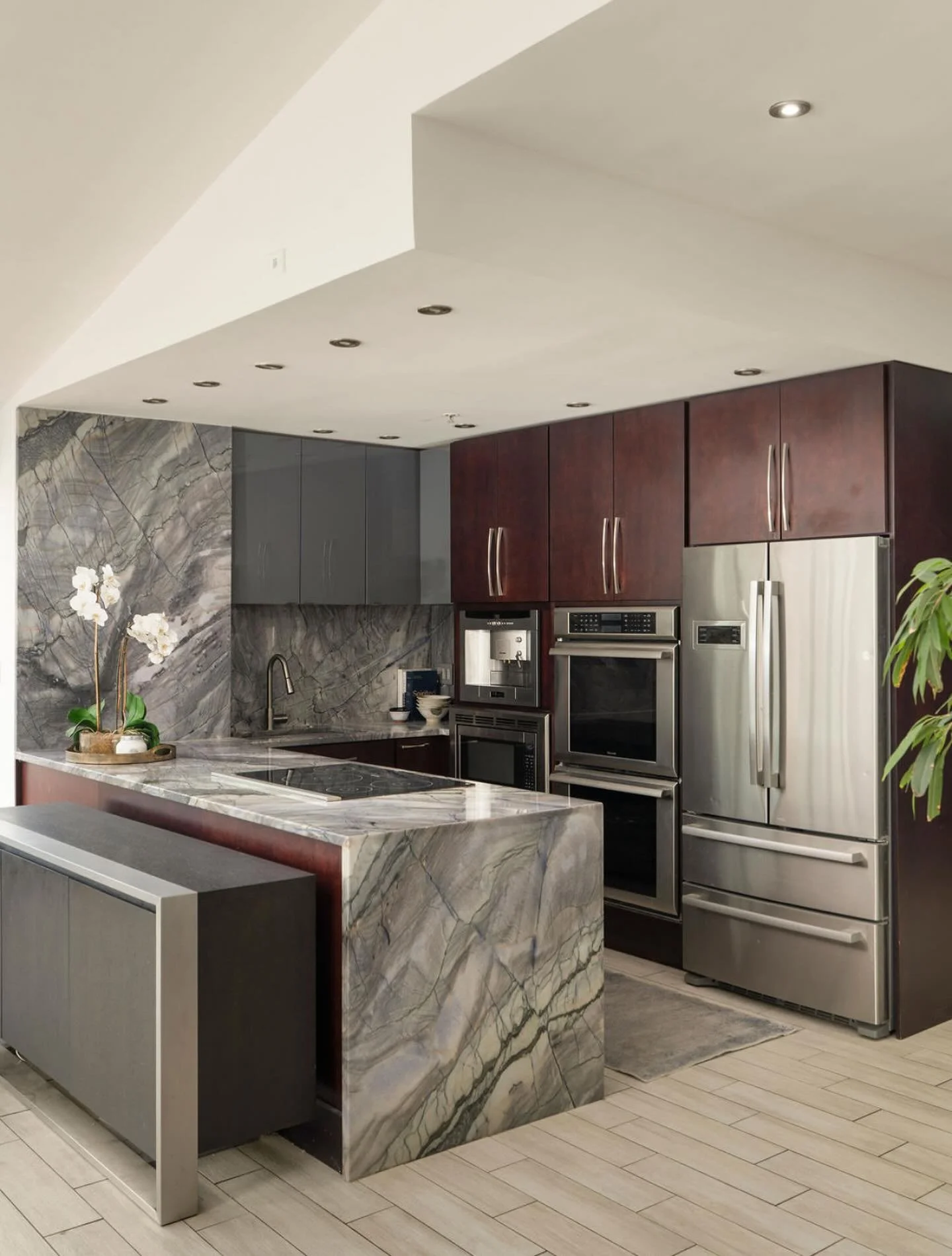 A double waterfall of Exotic Arizona Shadow Quartzite and two toned cabinets in a rich espresso stain and high gloss saturated gray grace this Penthouse on the Peninsula. 

This kitchen feels like home with every thoughtful touch, from custom storage