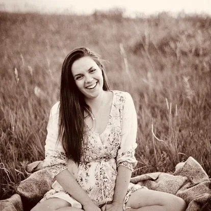 Smiling young woman sitting cross-legged outdoors in a grassy field.