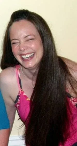 Woman with long dark hair smiling and wearing a pink dress.