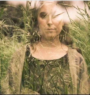 A woman standing in tall grass with trees in the background, with a semi-transparent double exposure effect.
