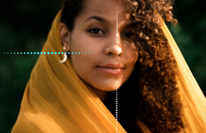 Close-up of a woman with curly hair wearing a yellow scarf and earrings, outdoors.