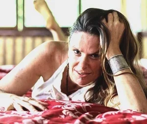 A woman lying on her side with a distressed expression, resting her head on her hand and holding her hair back.