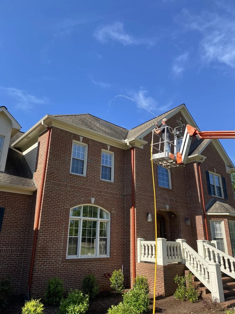 Apex Soft Wash cleaning a shingle roof on a brick home