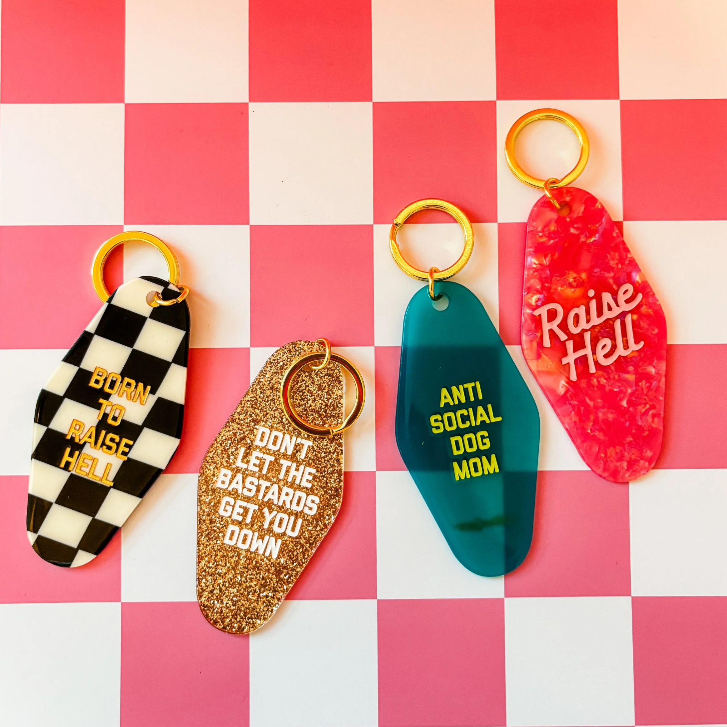 Collection of colorful keychains on a pink surface, some with phrases like 'go with your gut' and 'call your mom', with gold rings attached.
