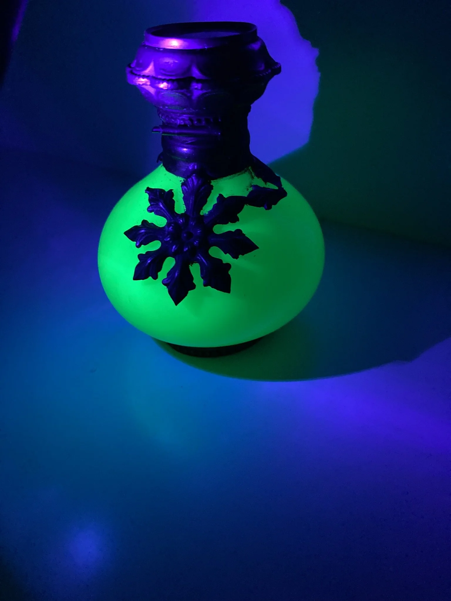 The same bottle photographed under ultraviolet light, the glass fluorescing bright green