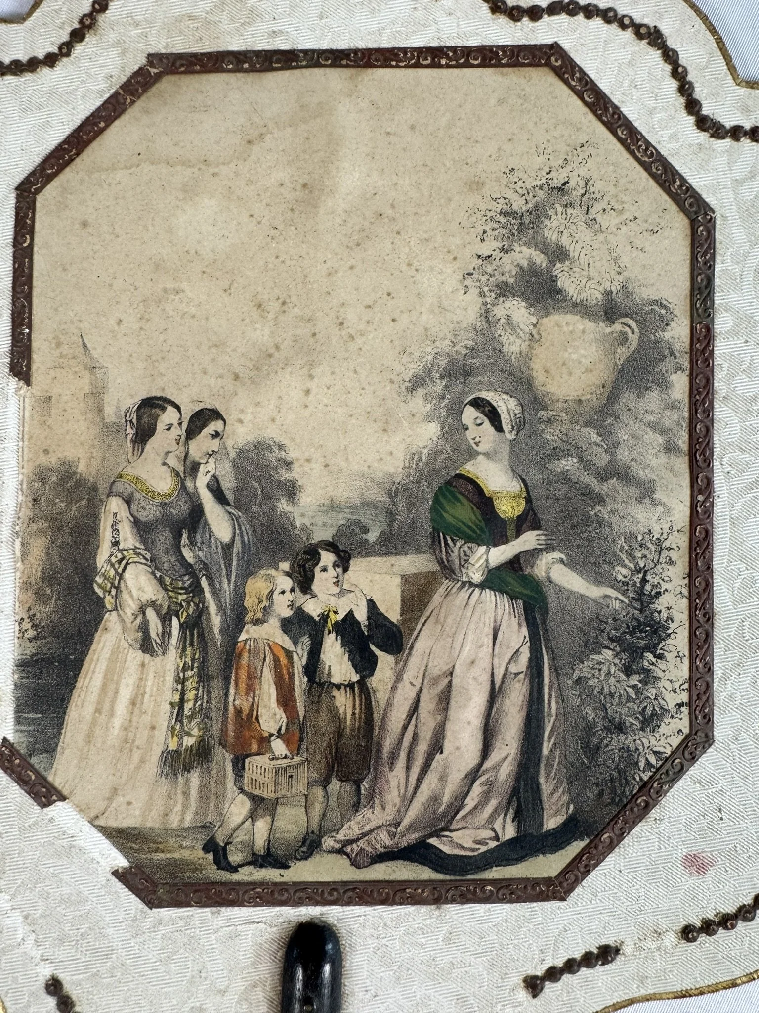 Detail of hand-coloured lithograph on antique French fire screen, ecran a main, Romantic period c.1840, garden genre scene with elegantly dressed women and children, octagonal gilt reserve