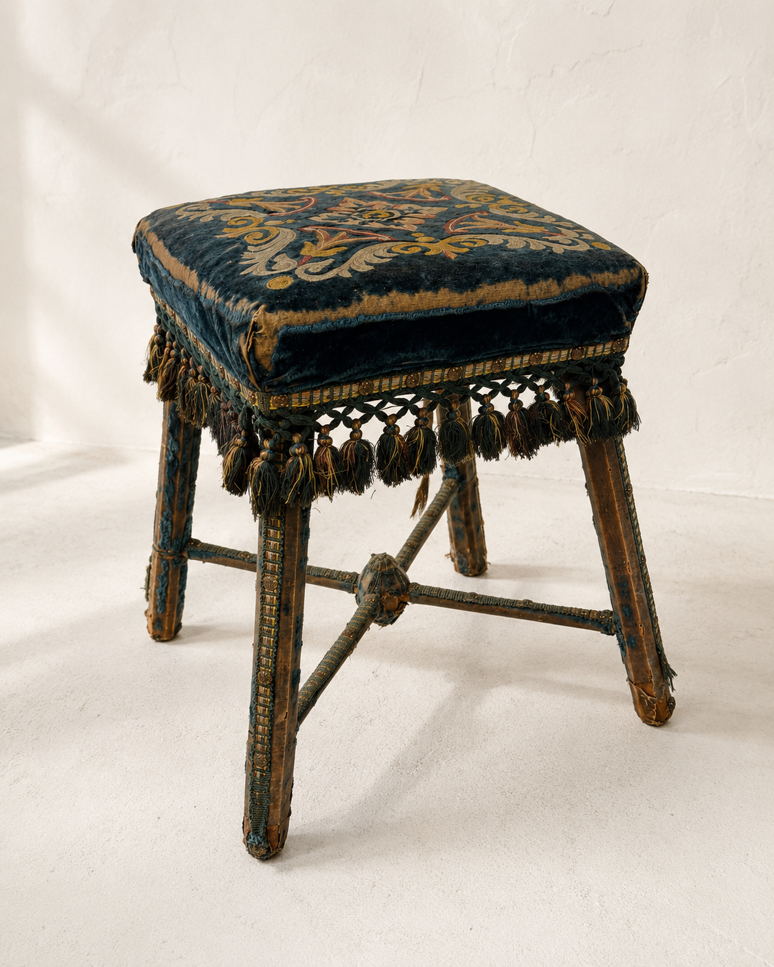 Blue velvet upholstered stool with tassel fringe and X stretcher