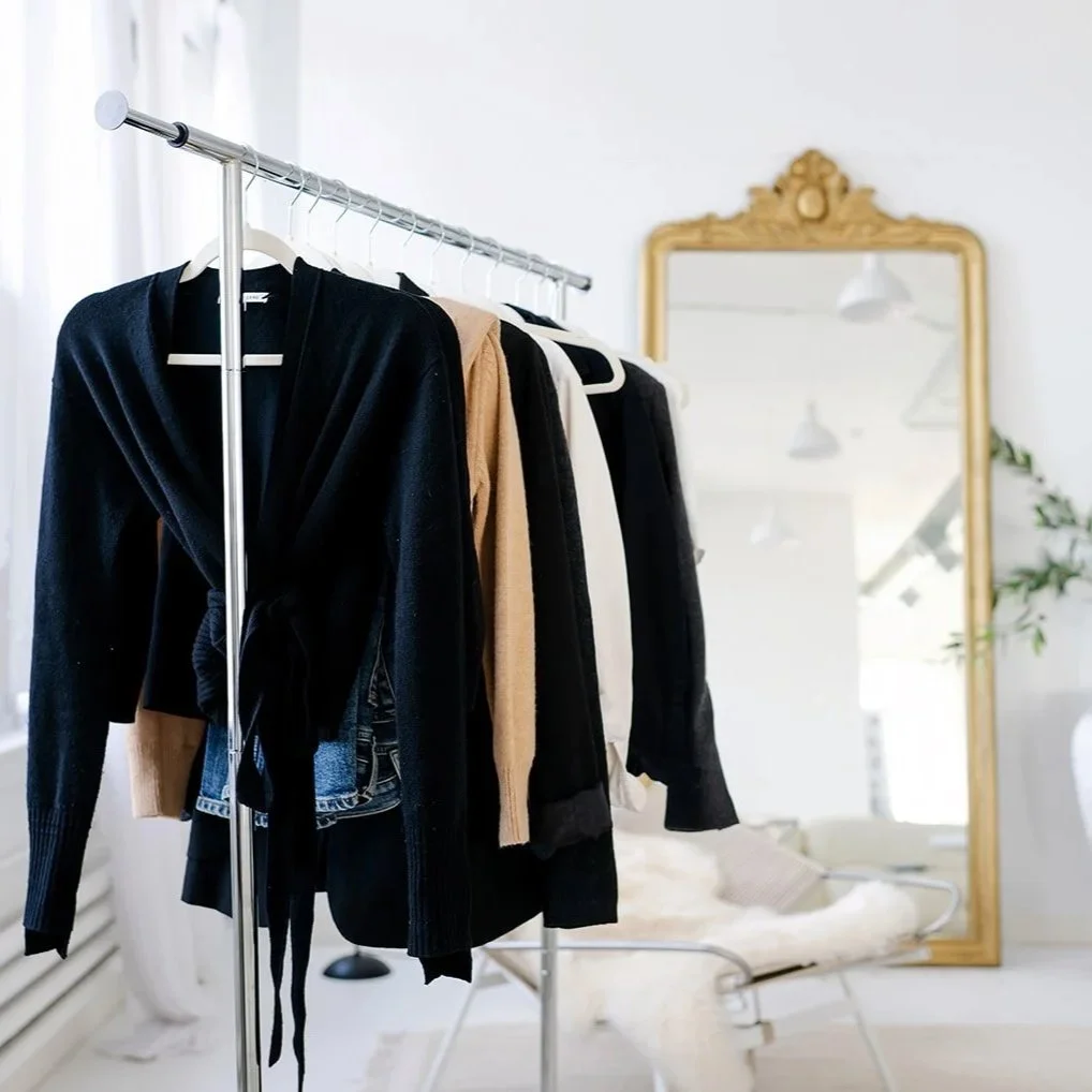 Clothes hanging on a metal rack in front of a mirror in a bright, minimalistic room.