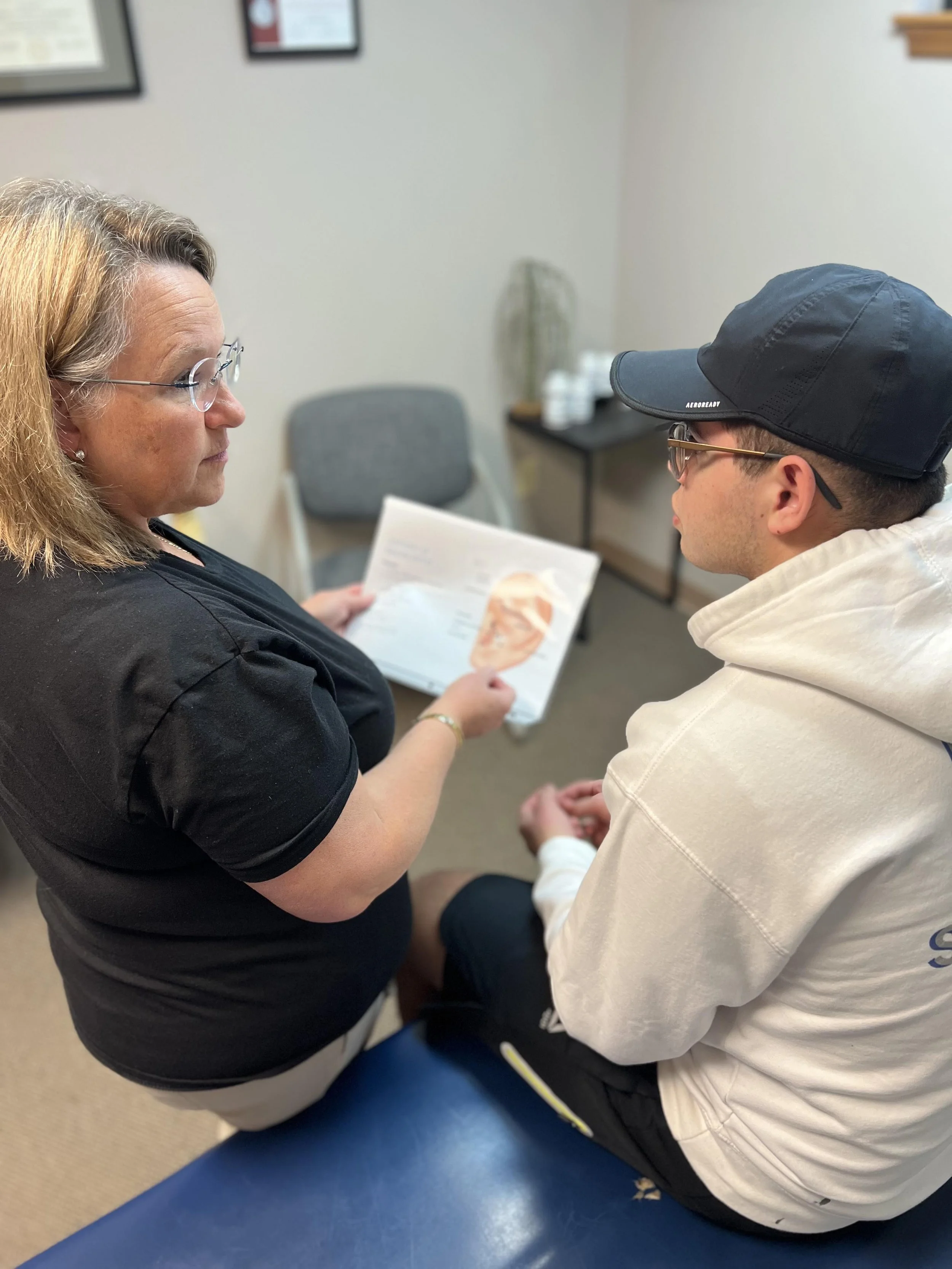 A female healthcare professional smiling and holding a folder, talking to an older female patient in a medical office.