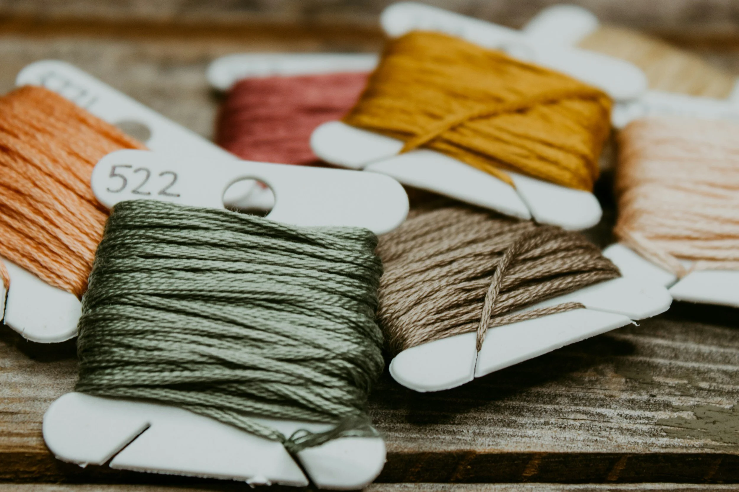 Multiple spools of embroidery thread in various colors on a wooden surface.