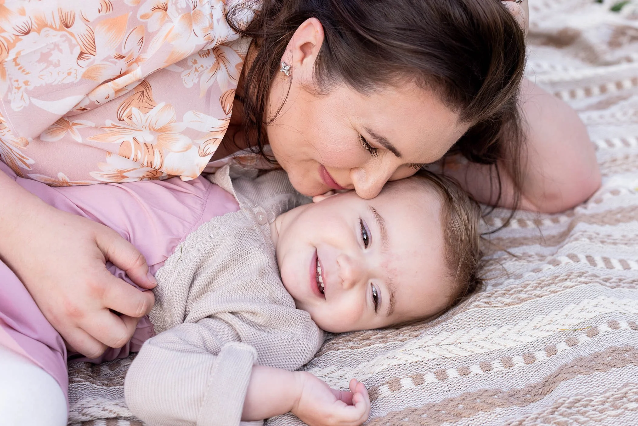 Mom and giggly daughter cuddle on blanket wearing spring colors