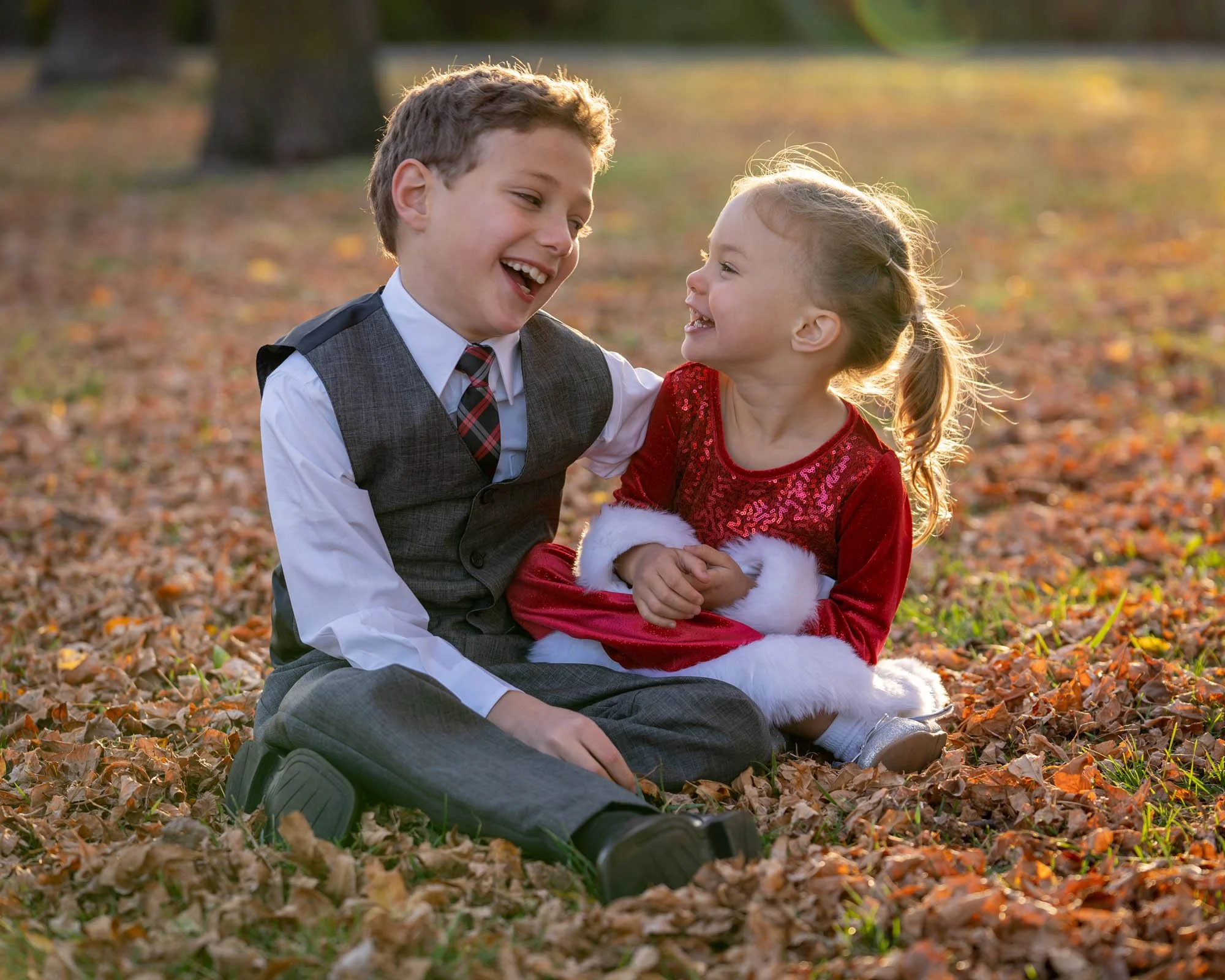 Young brother and sister sitting together giggling at each other surrounded by pretty fall colored leaves showing joy and happiness