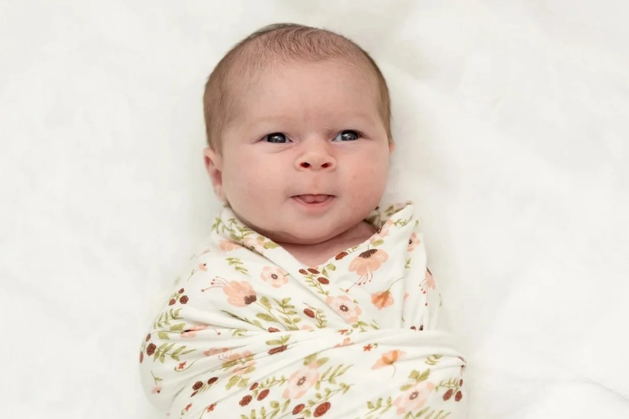 newborn+baby+wrapped+in+floral+swaddle+laying+on+white+blanket.jpg