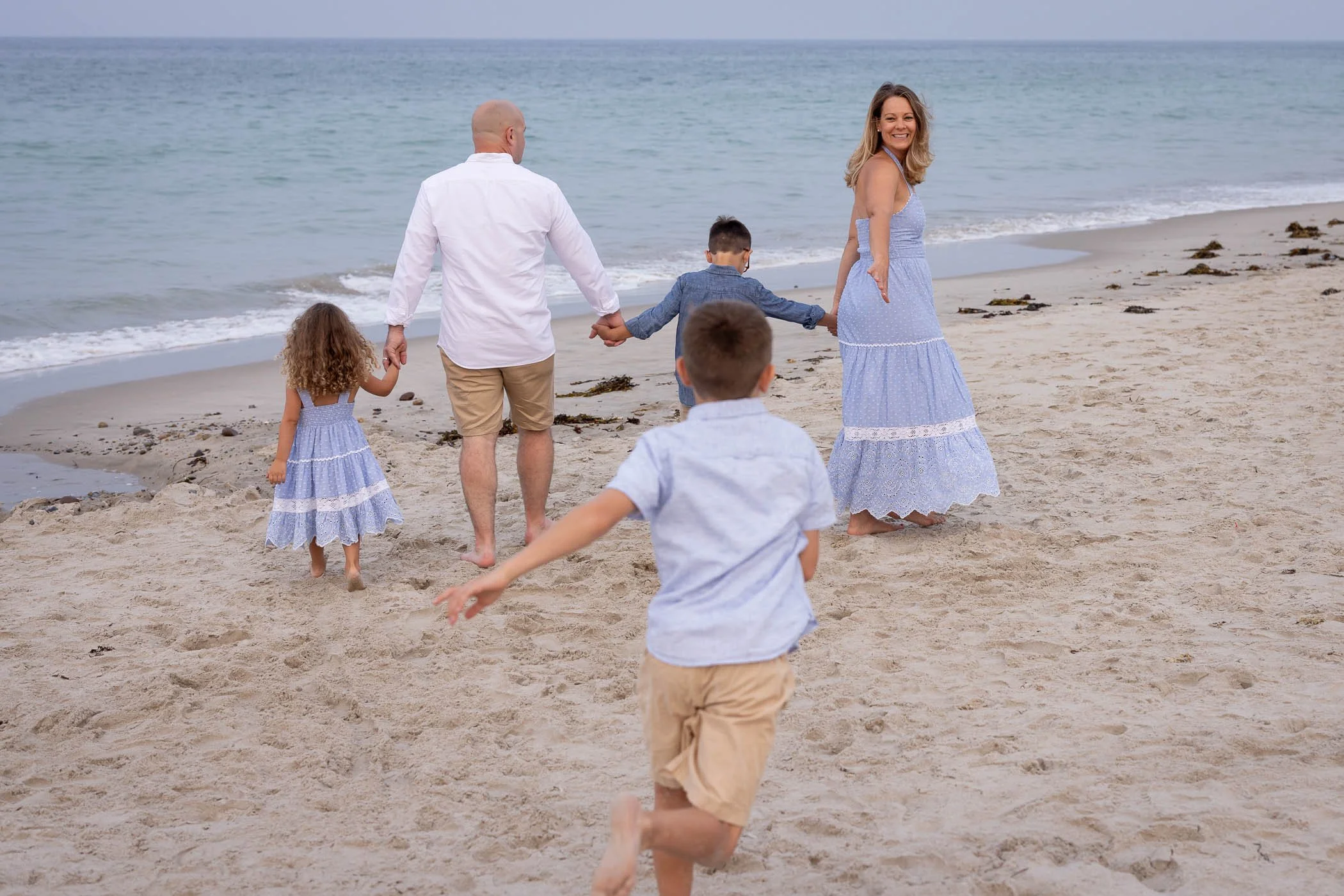Young boy runs toward mom, dad, and siblings on beach