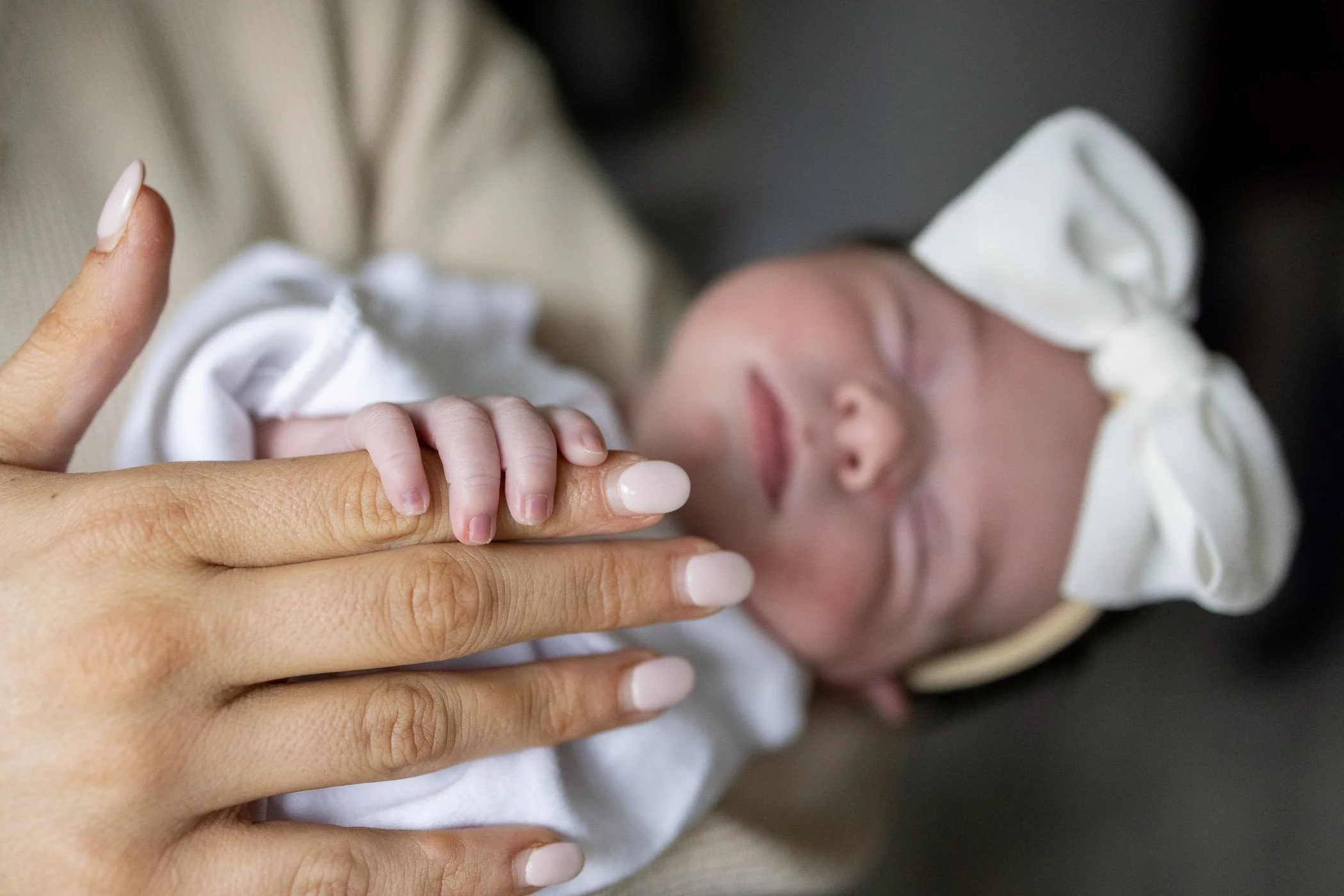 Baby fingers wrapped around mom's index finder sleeping in her arms