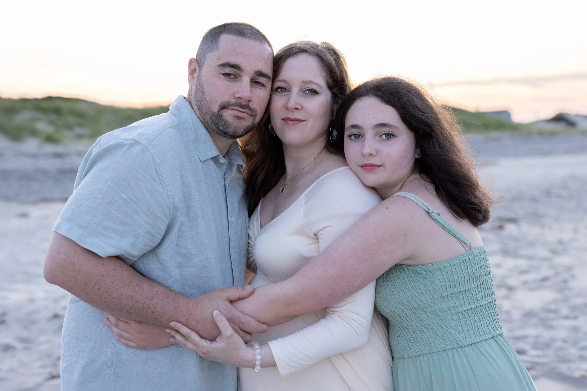 husband-pregnant-wife-and-daugher-embrace-on-beach-showing-love.jpg