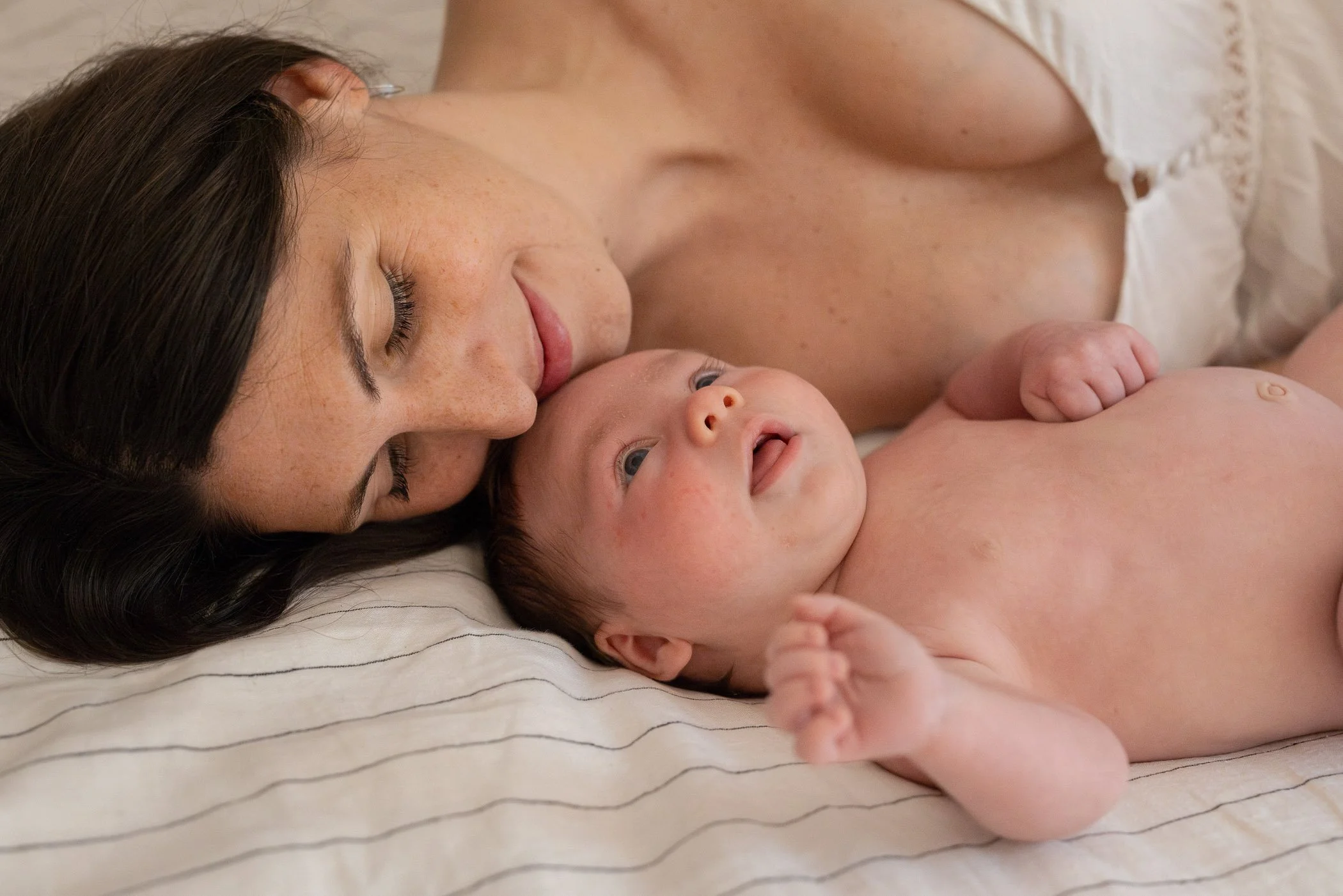 Mom laying on bed snuggling close to newborn son looking up at her showing love and connection
