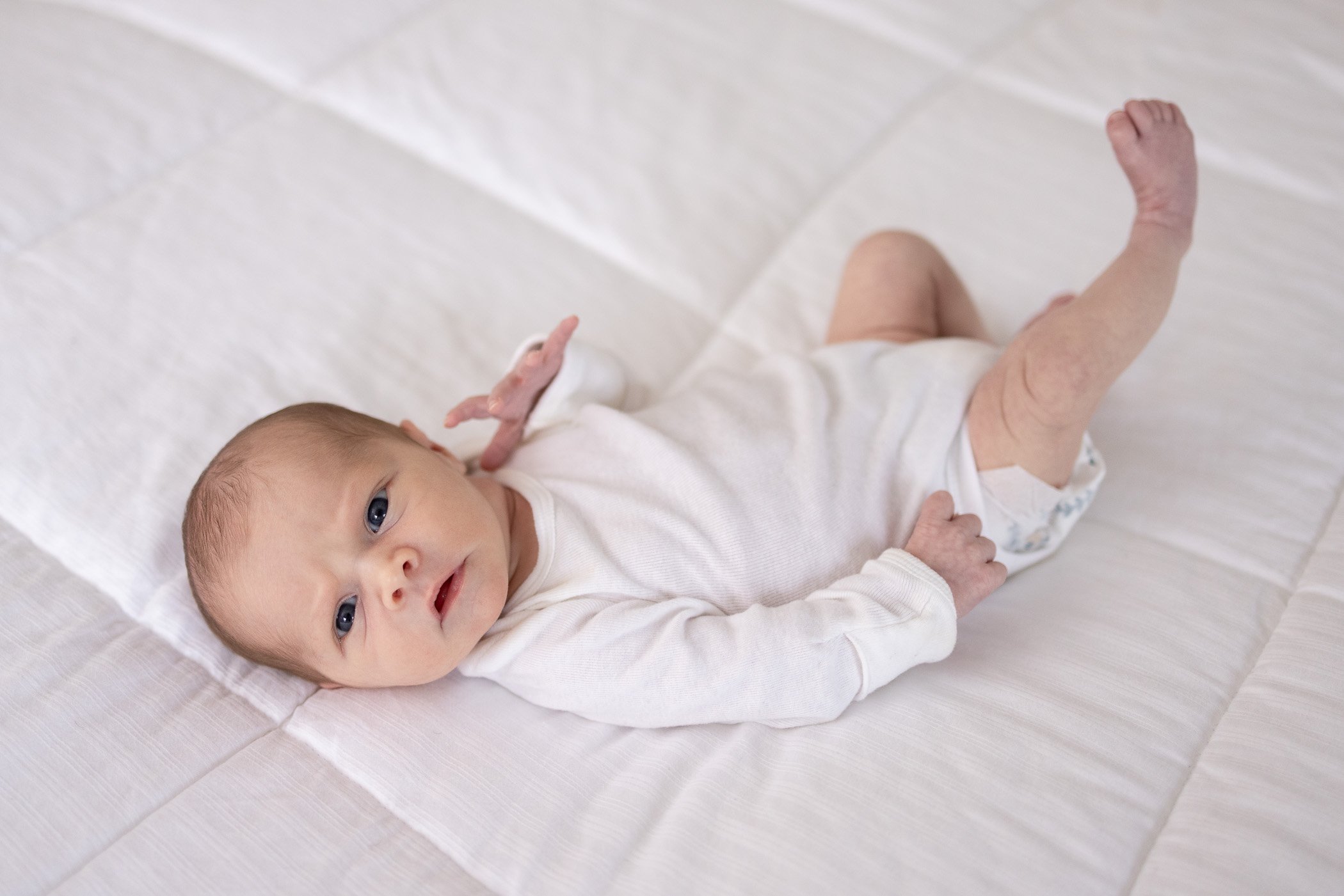 Newborn baby girl on bed looking at camera with one leg up