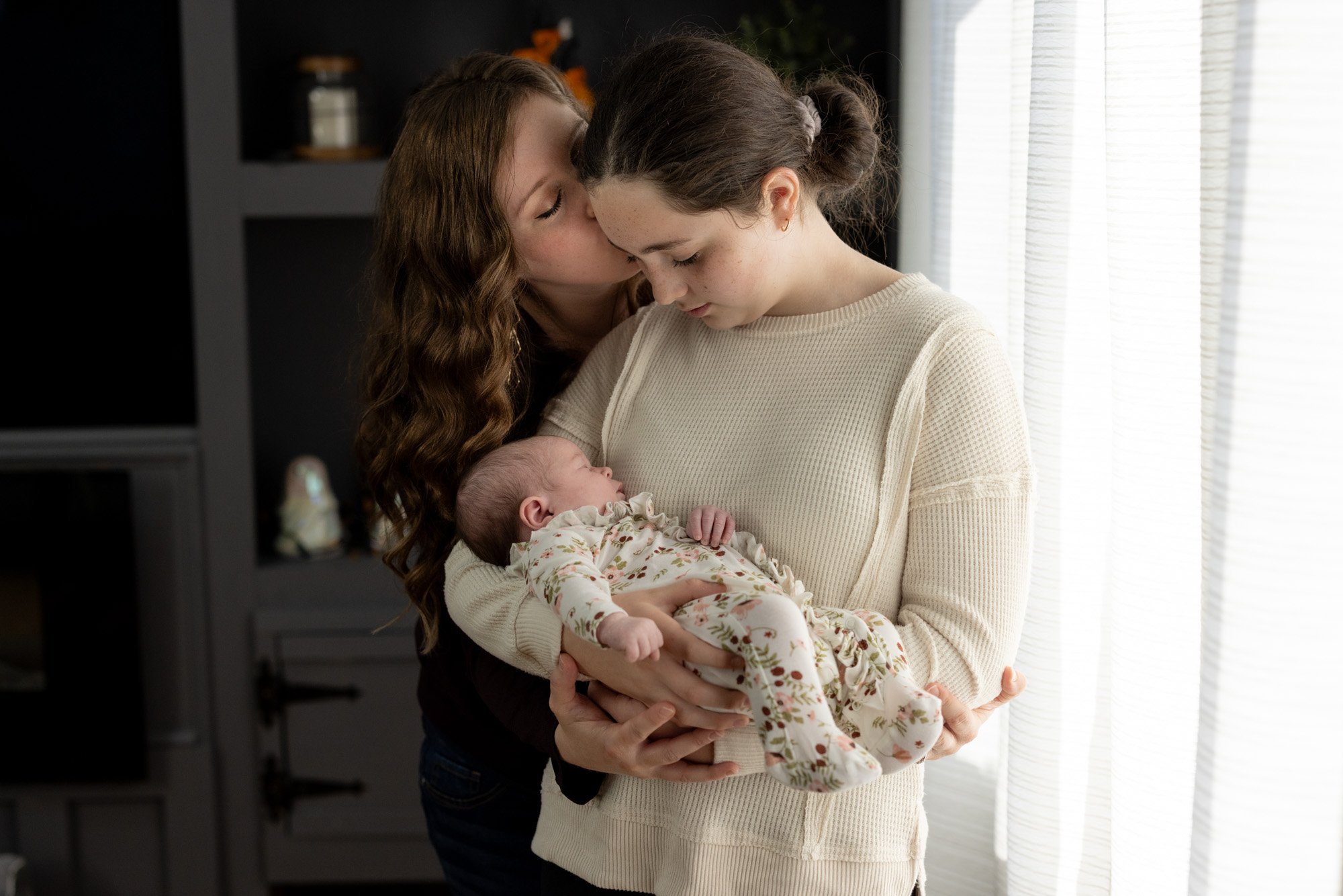 mom kisses older daughter holding newborn sister.jpg