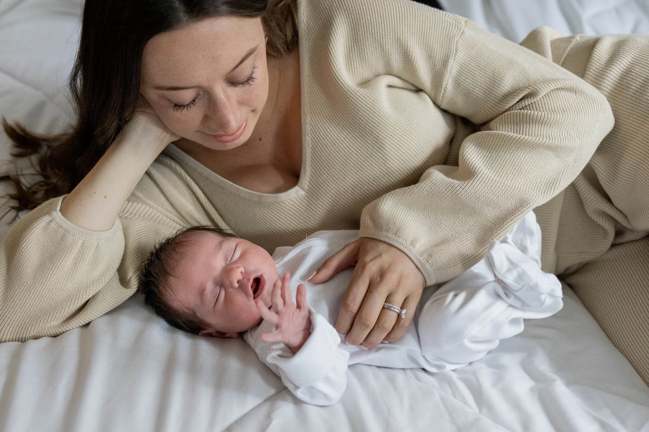 Mama comforts newborn daughter on bed during