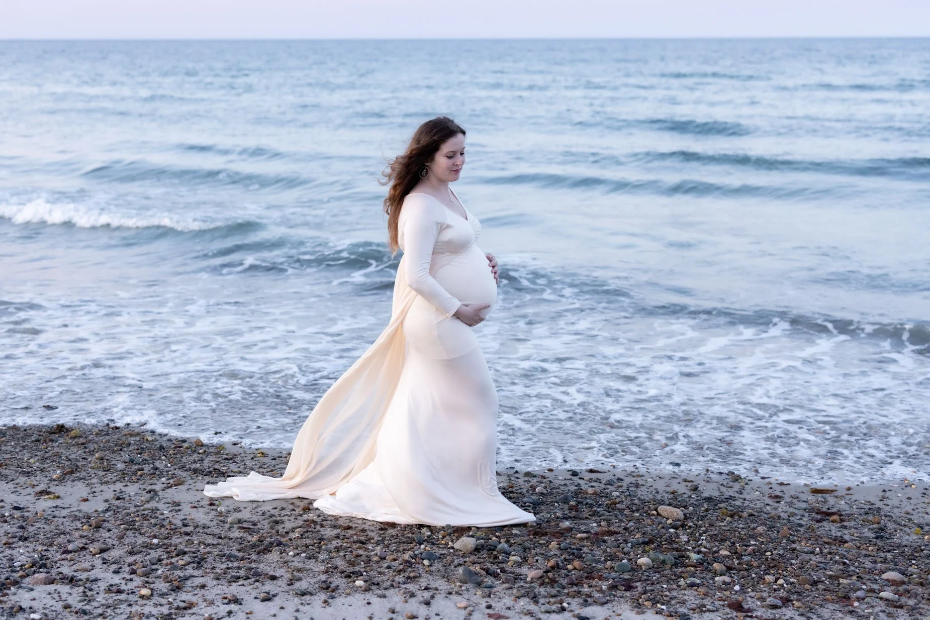 pregnant woman walks along ocean holding baby bump