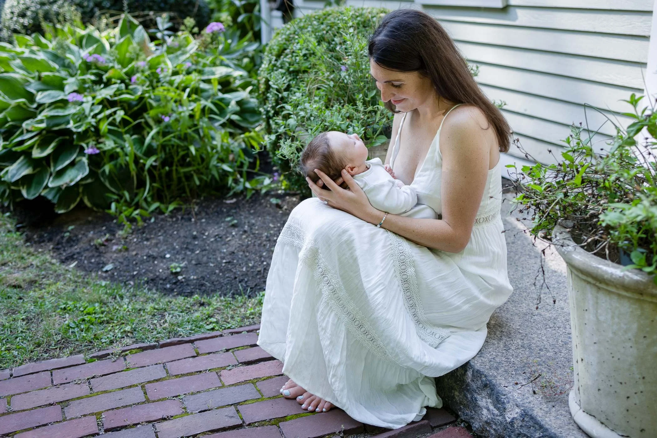 Mom wearing elegant white dress cradles baby boy on front step