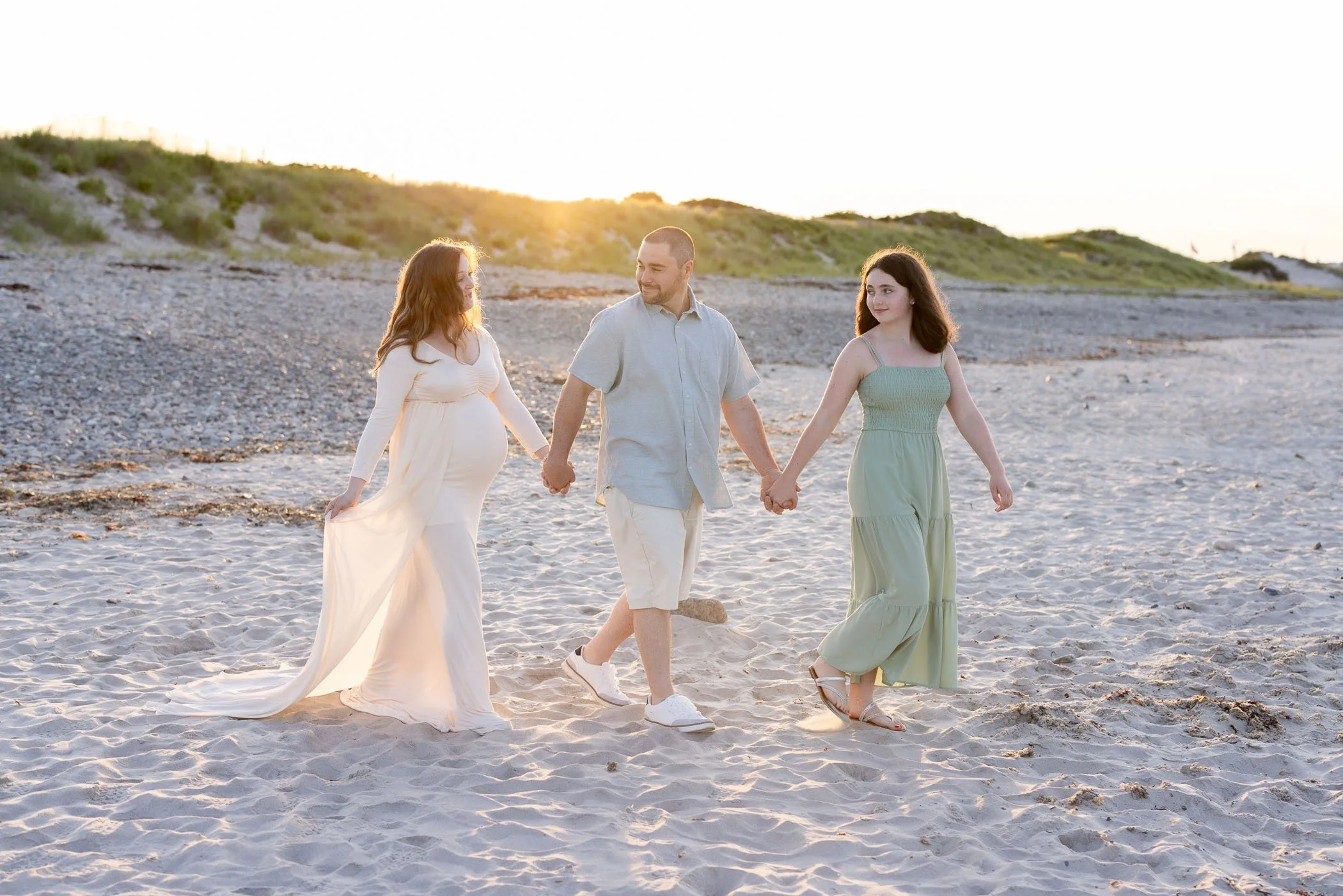 Pregnant wife husband daughter walk on beach at sunset