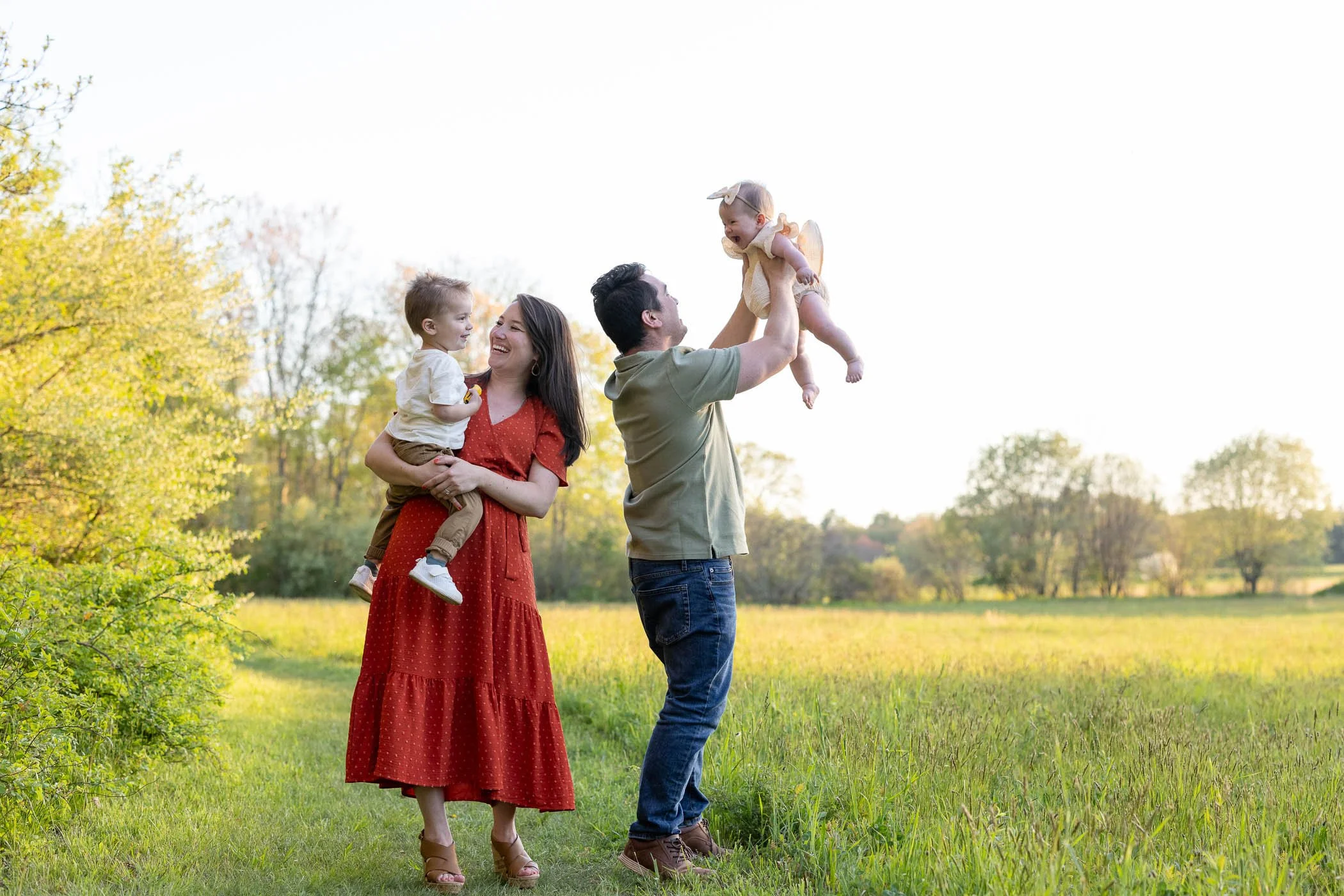 Mom holds son dad tossed daughter in air in pretty field
