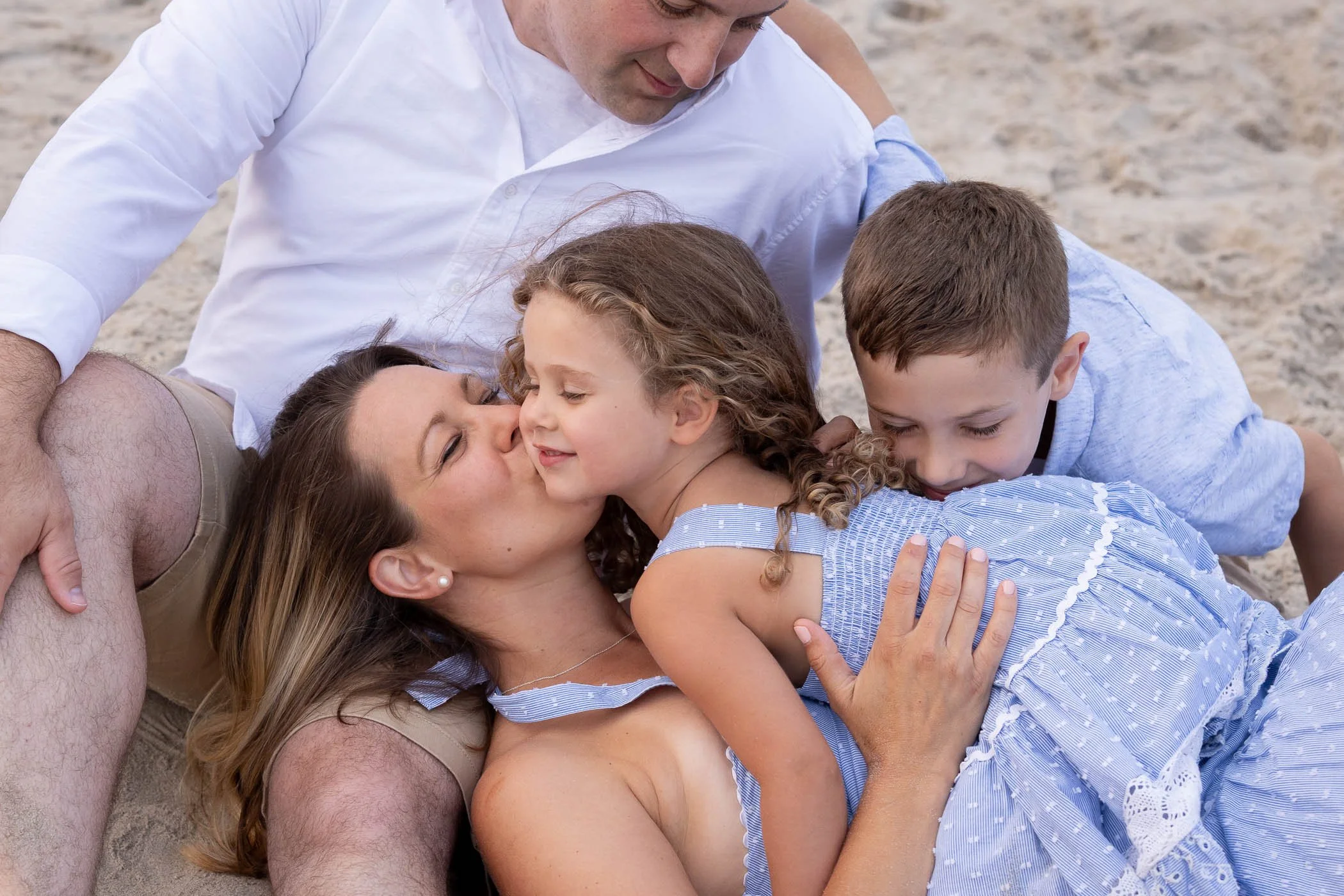 Family cuddles on beach mom kisses daughter tenderly