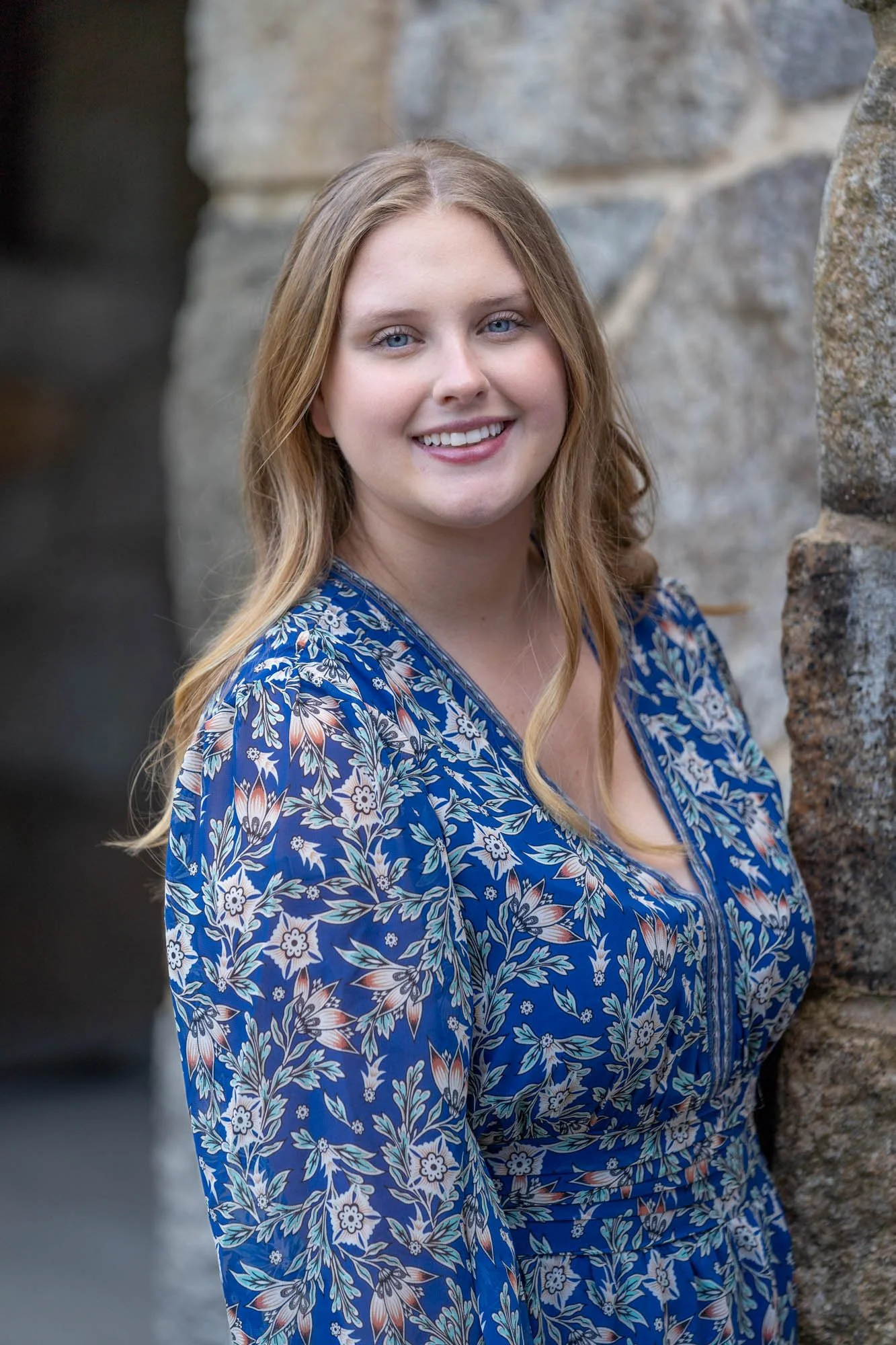 High school female wearing blue dress near stone wall