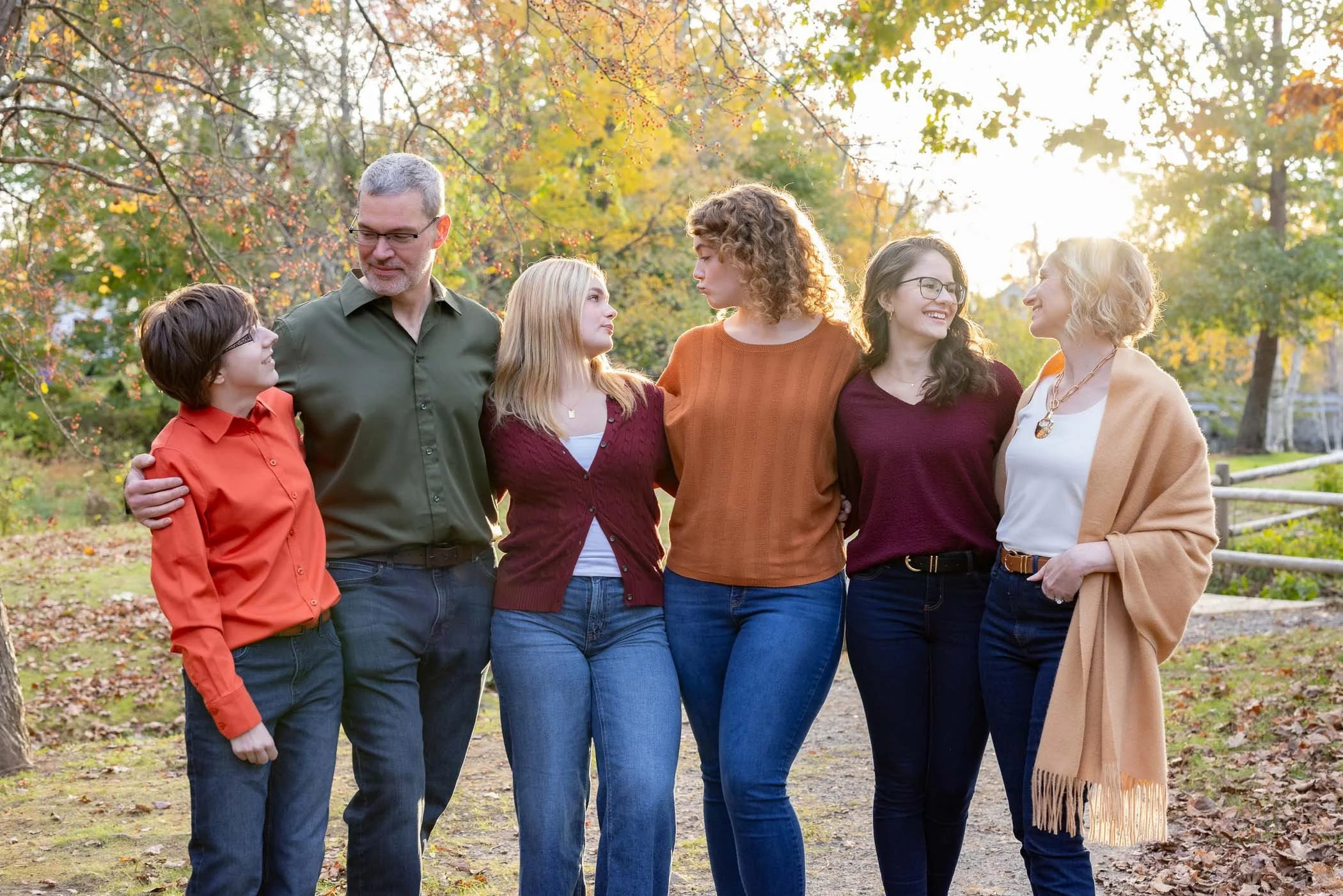 Family of 6 embrace and look at each other in a park with fall colors