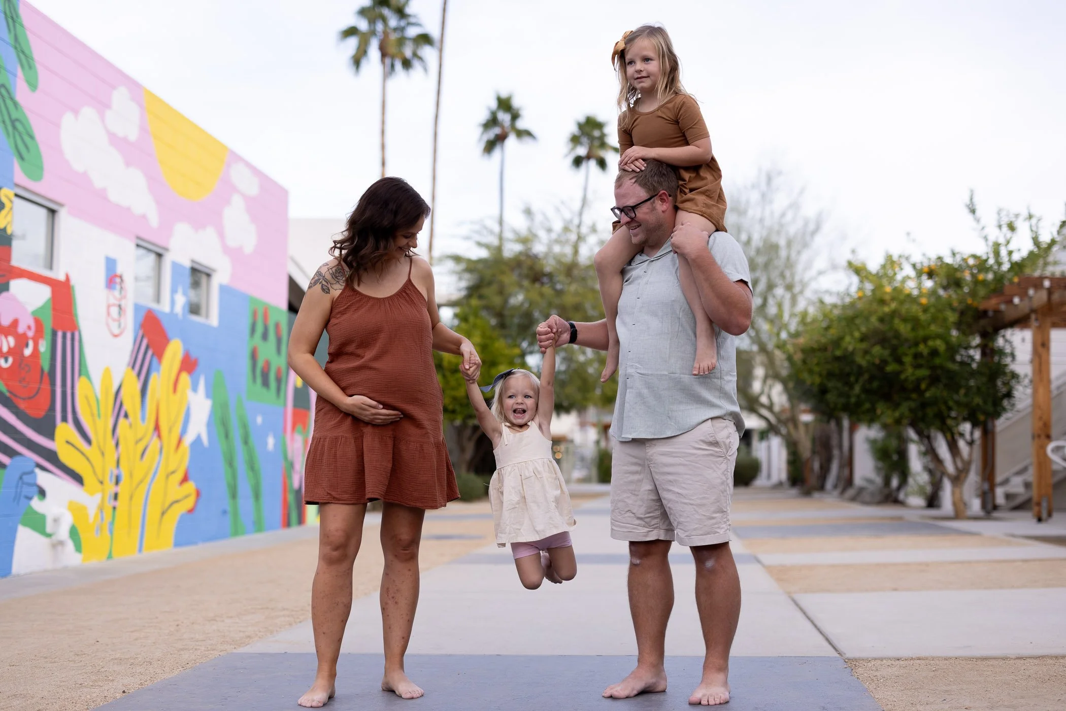 Pregnant wife and husband swing daughter with child on his shoulders