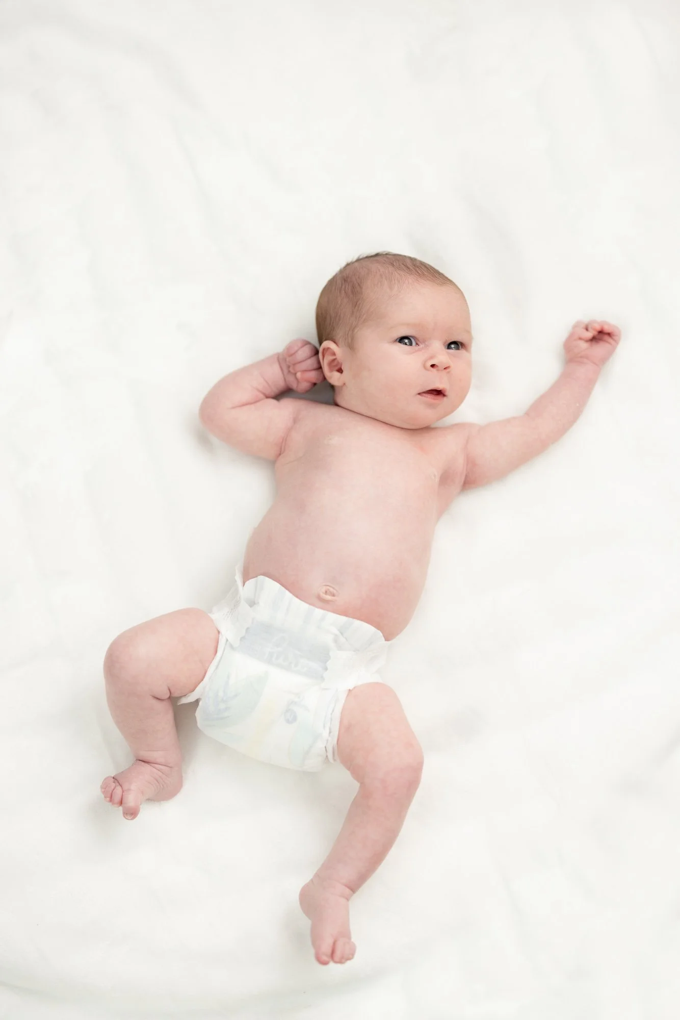 newborn baby girl in diaper laying on white blanket.jpg