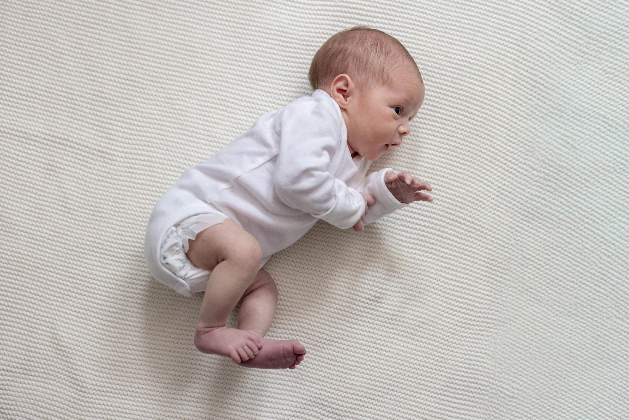 Wide awake newborn baby girl laying on her side wearing white onesie